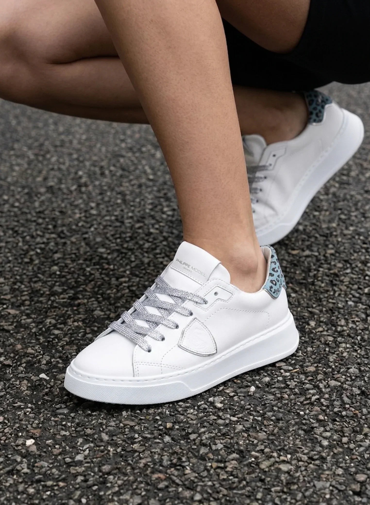 Sneakers bianche da donna con dettagli animalier azzurri sul tallone, stile casual su asfalto