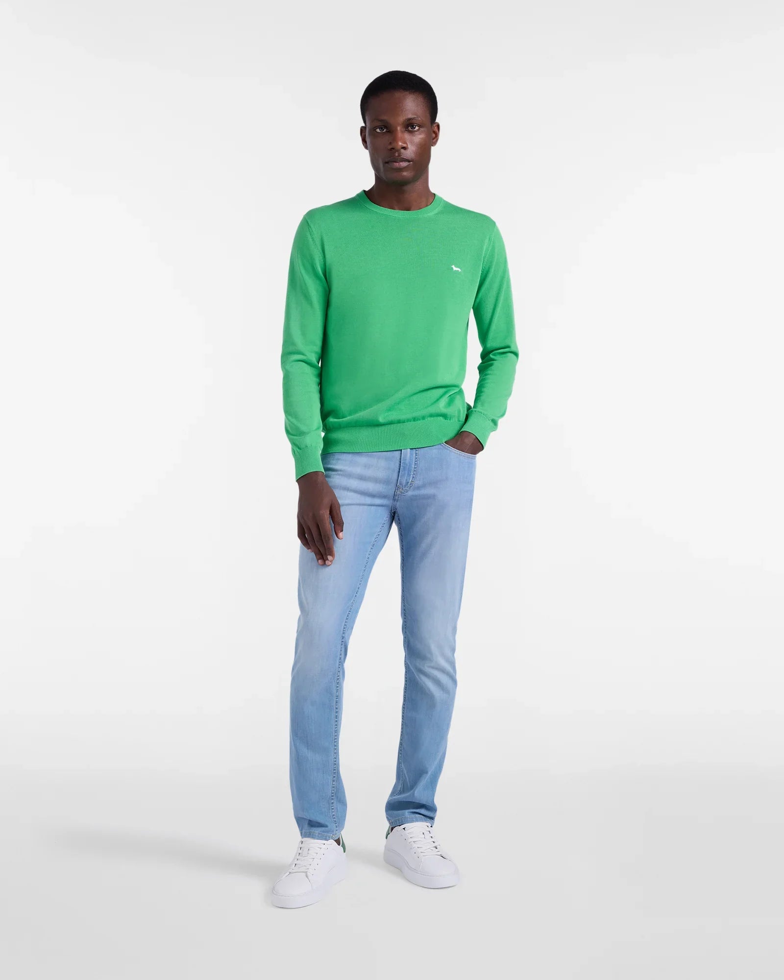 Uomo con maglione verde, jeans chiari e sneakers bianche su sfondo bianco