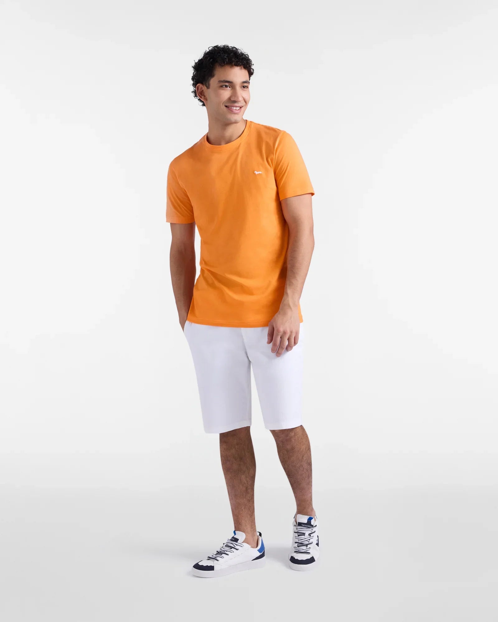 Uomo con t-shirt arancione, bermuda bianchi e sneakers, moda estiva casual uomo