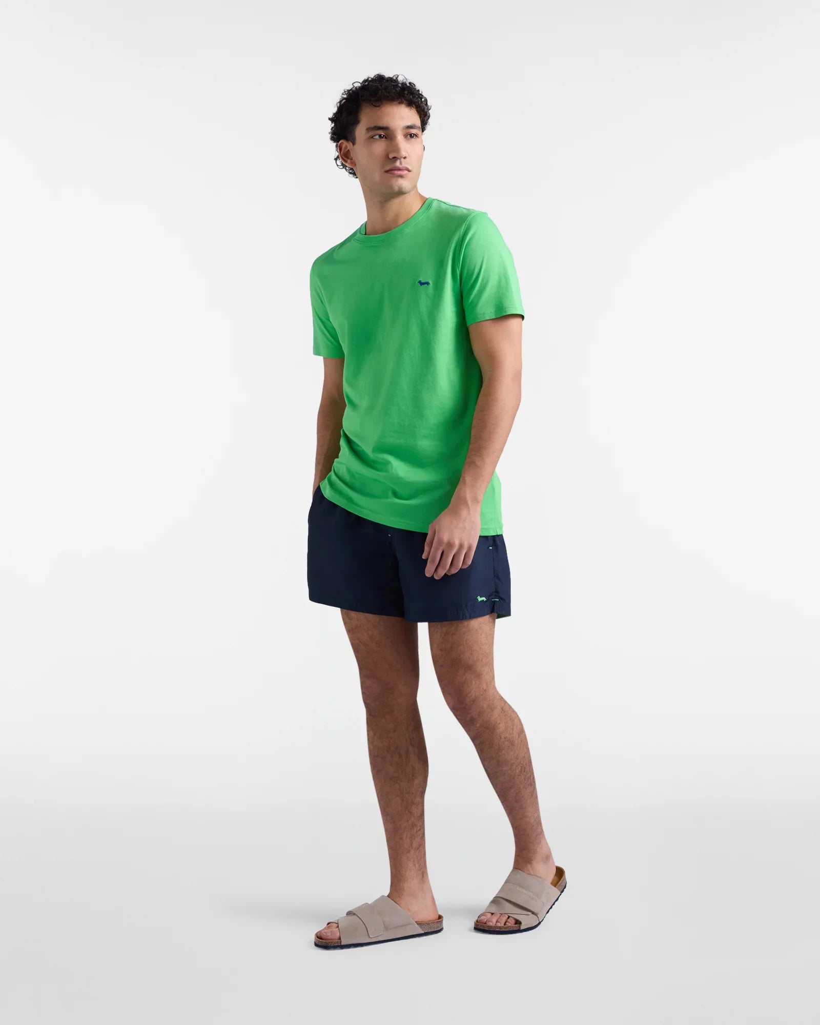 Uomo con t-shirt verde, pantaloncini blu e sandali beige, moda casual estiva