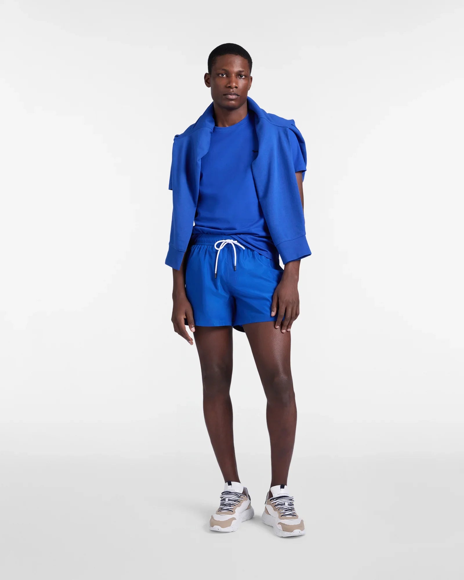 Modello indossa completo sportivo blu con t-shirt, pantaloncini e sneakers moda uomo
