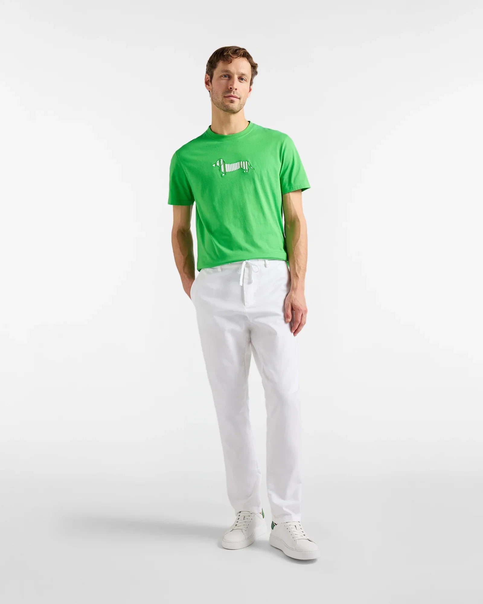 Uomo con t-shirt verde con cane stampato, pantaloni bianchi e sneakers bianche, moda casual