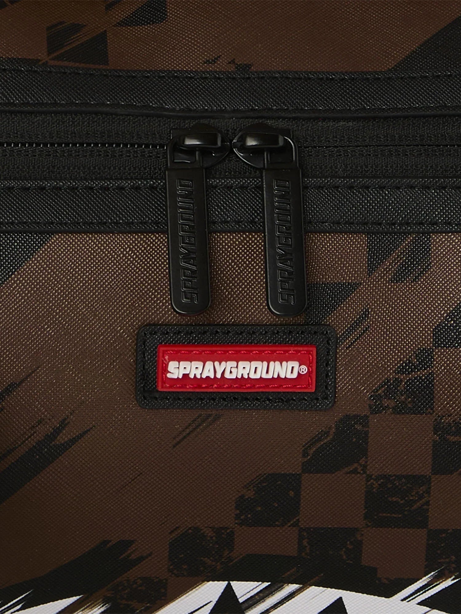 Dettaglio zaino Sprayground marrone con motivo geometrico, doppia zip e logo visibile.
