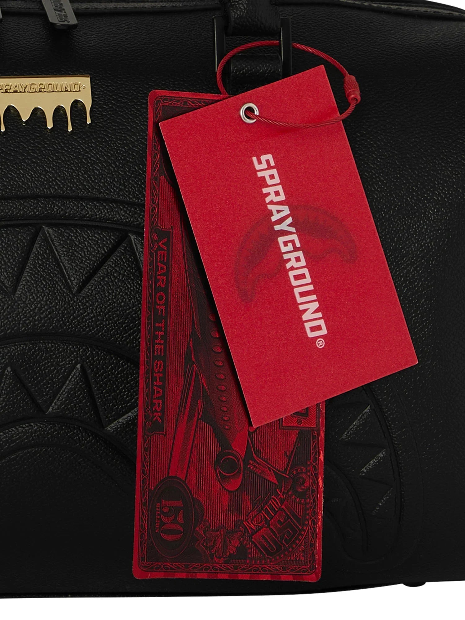 Dettaglio borsa nera Sprayground con etichetta rossa, scritta, texture effetto squalo.
