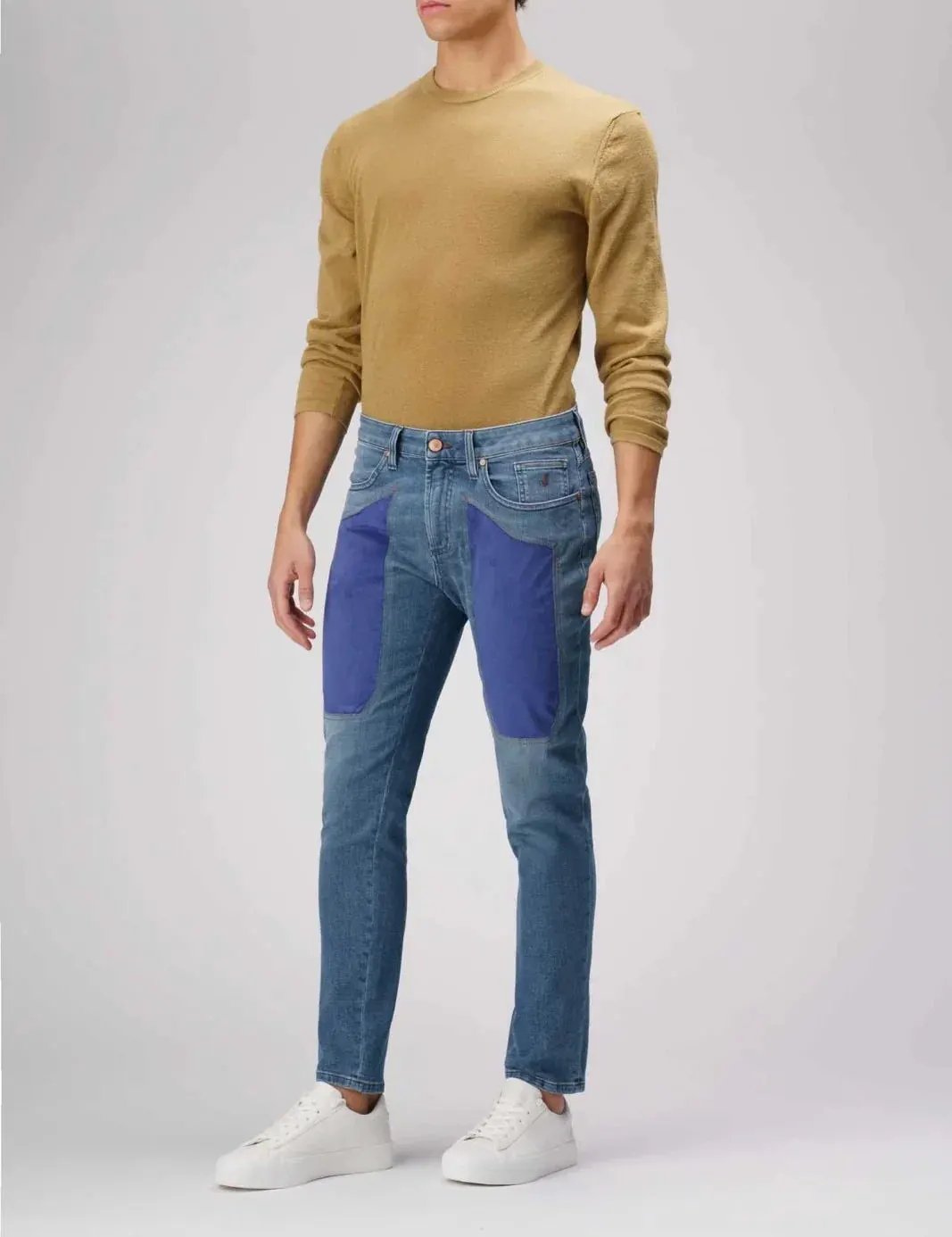 Modello indossa jeans slim fit patchwork blu e maglia beige, abbigliamento uomo casual.