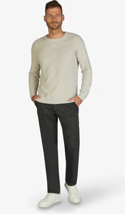 Modello indossa maglione beige, pantaloni neri e sneakers bianche, moda uomo casual elegante.