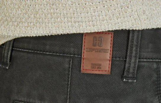 Dettaglio jeans uomo Club+Comfort grigi con etichetta in pelle e maglia beige in primo piano.