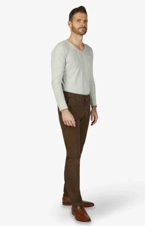 Modello indossa pantaloni uomo marroni, camicia grigia, scarpe cuoio, stile elegante.