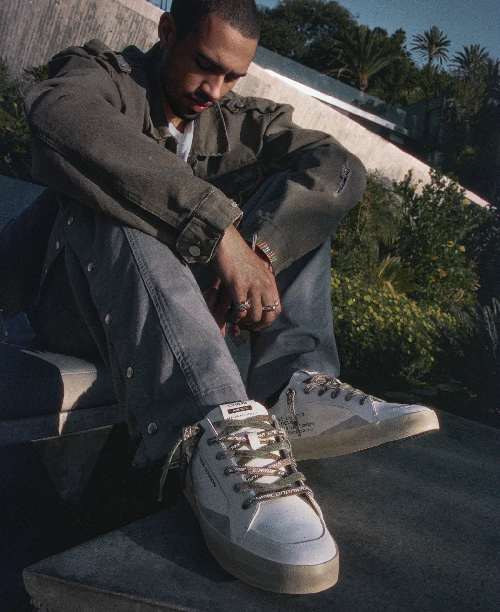 Uomo con giacca verde e pantaloni grigi indossa sneakers bianche di tendenza all'aperto, moda uomo.