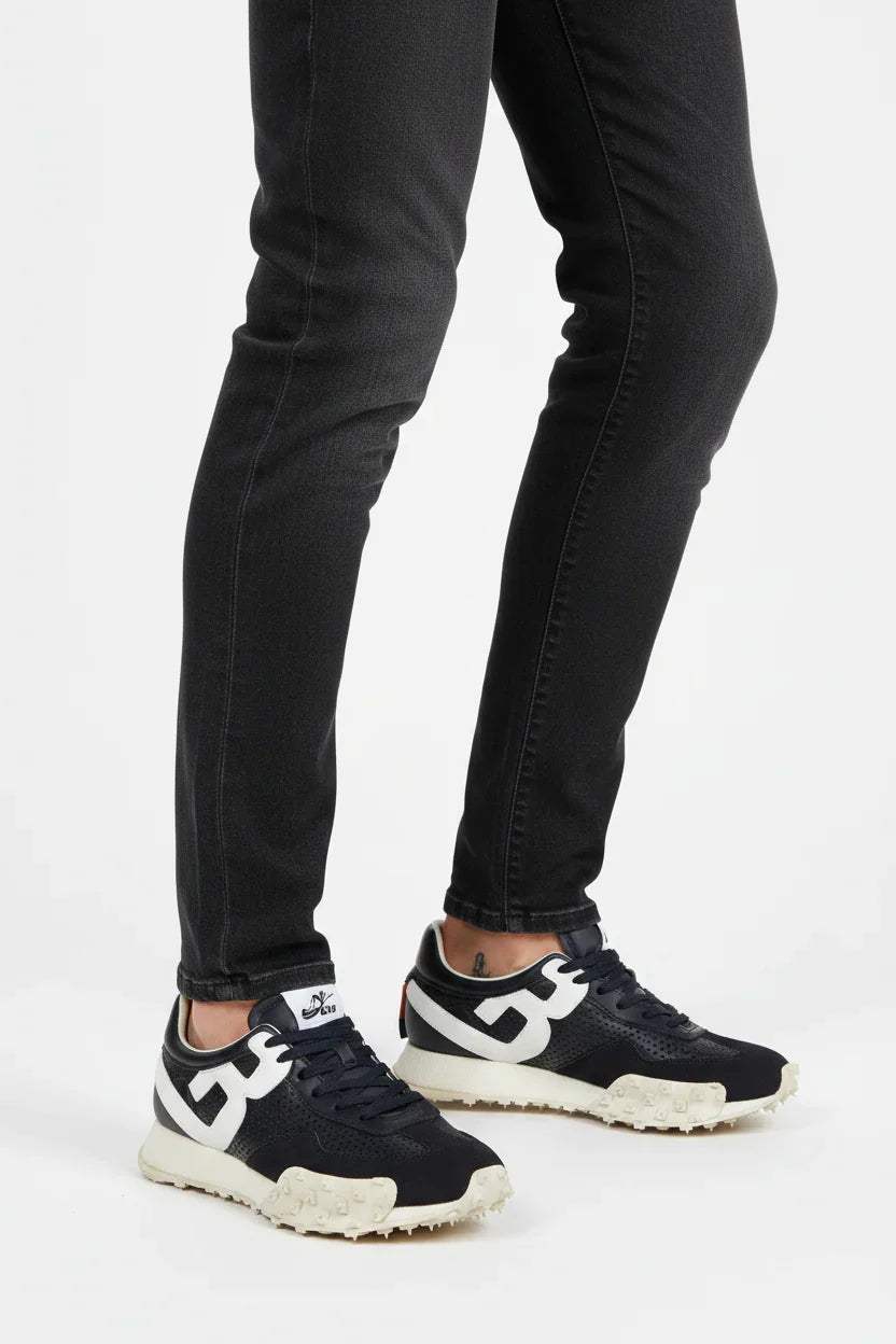 Sneakers uomo nere e bianche con suola carrarmato, indossate con jeans neri.