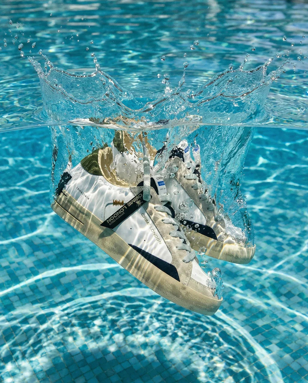 Scarpe sportive bianche e beige che cadono nell'acqua di una piscina, spruzzi evidenti.