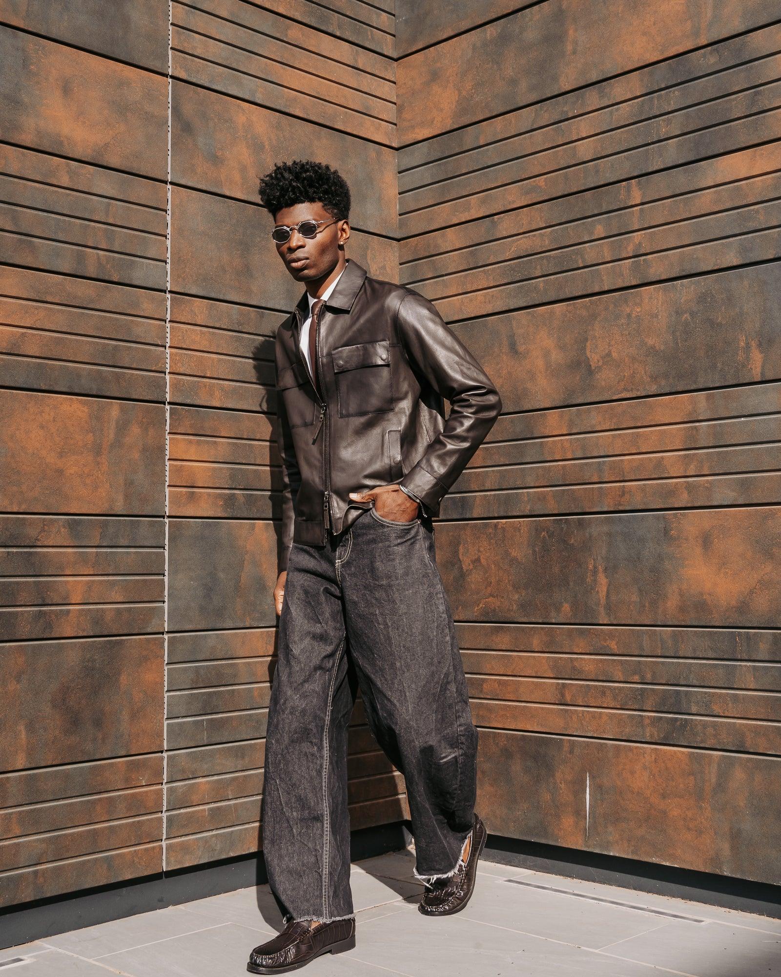 Uomo con giacca in pelle marrone, jeans larghi e mocassini, look moda uomo urbano