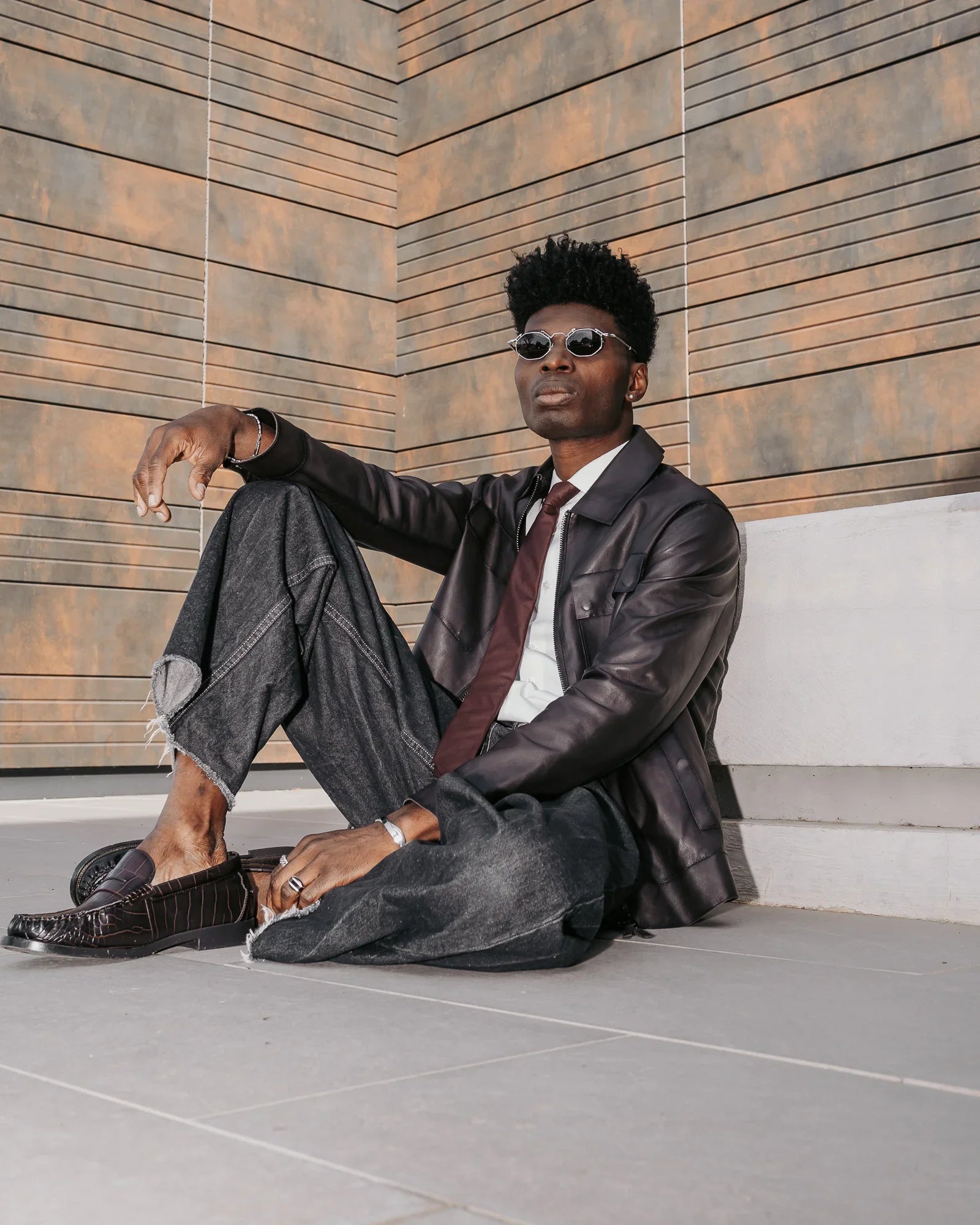Modello uomo con giacca in pelle, jeans larghi e mocassini, stile moda urbana elegante.