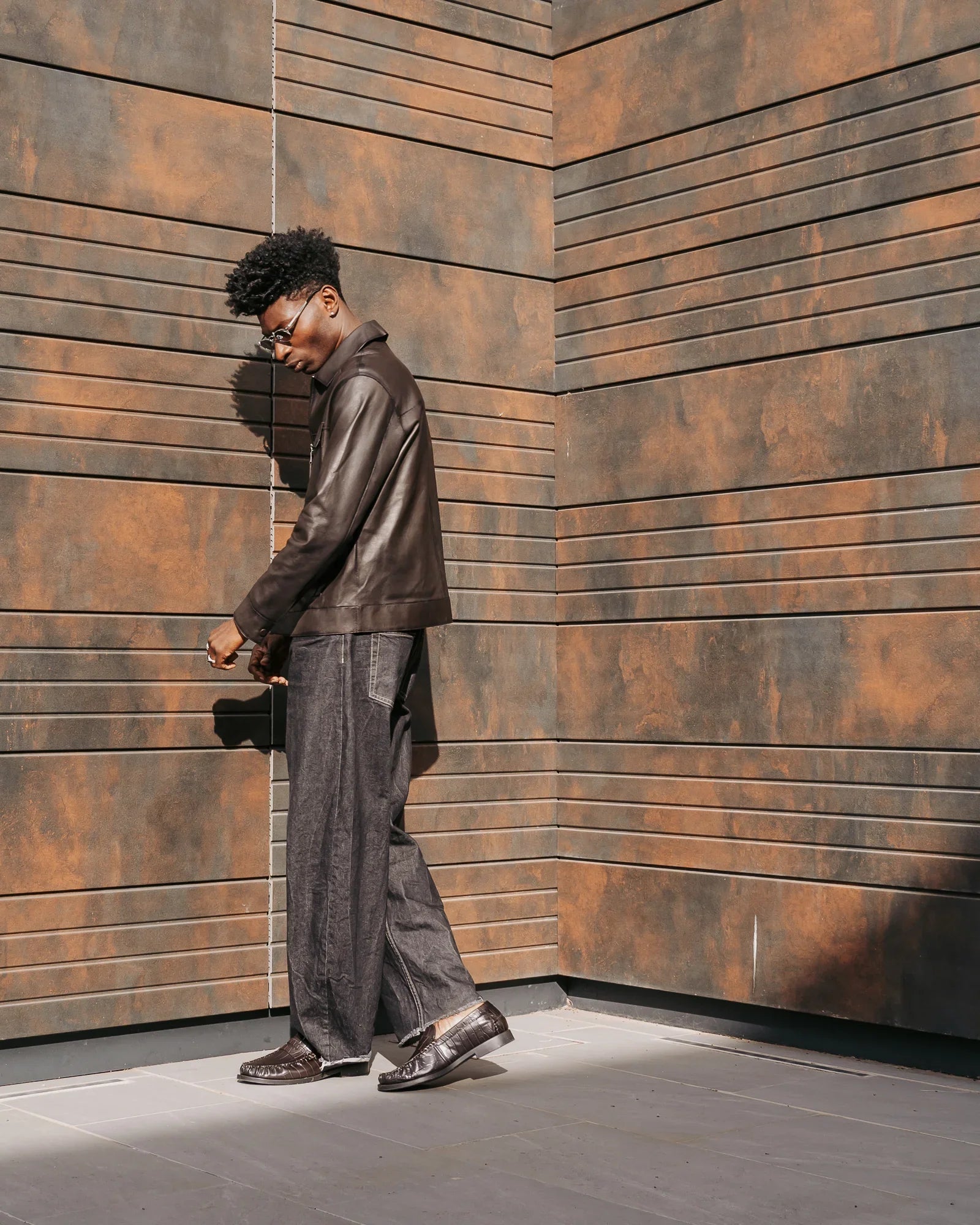 Uomo con giacca in pelle nera, jeans larghi e mocassini, look moda uomo elegante urbano.
