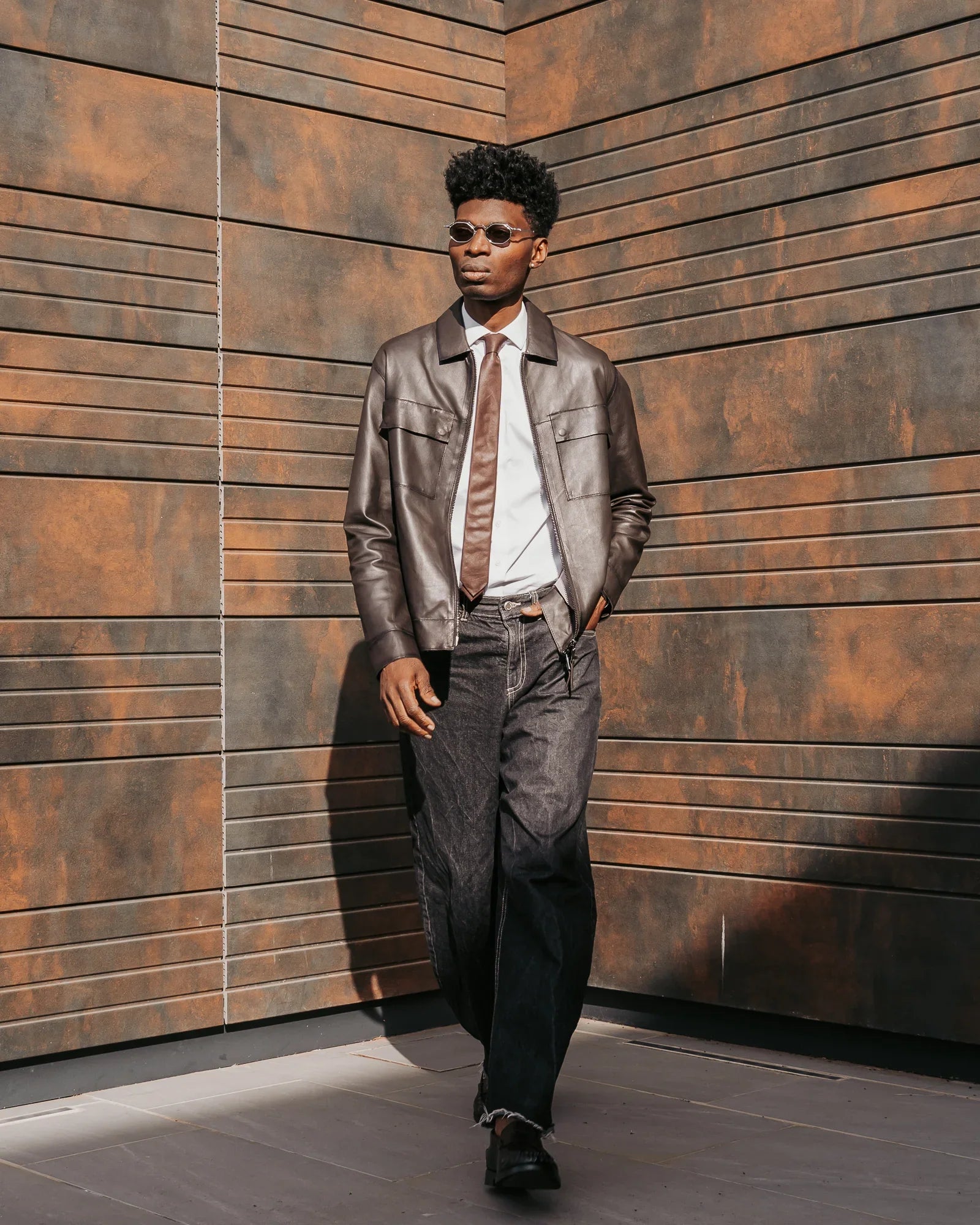 Uomo con giacca di pelle marrone, camicia bianca e jeans scuri, stile elegante casual.