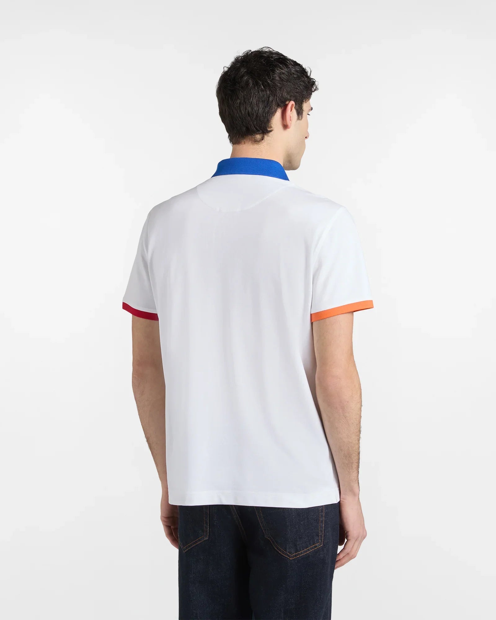Uomo di schiena con polo bianca, colletto blu, bordi maniche arancione e rosso, jeans