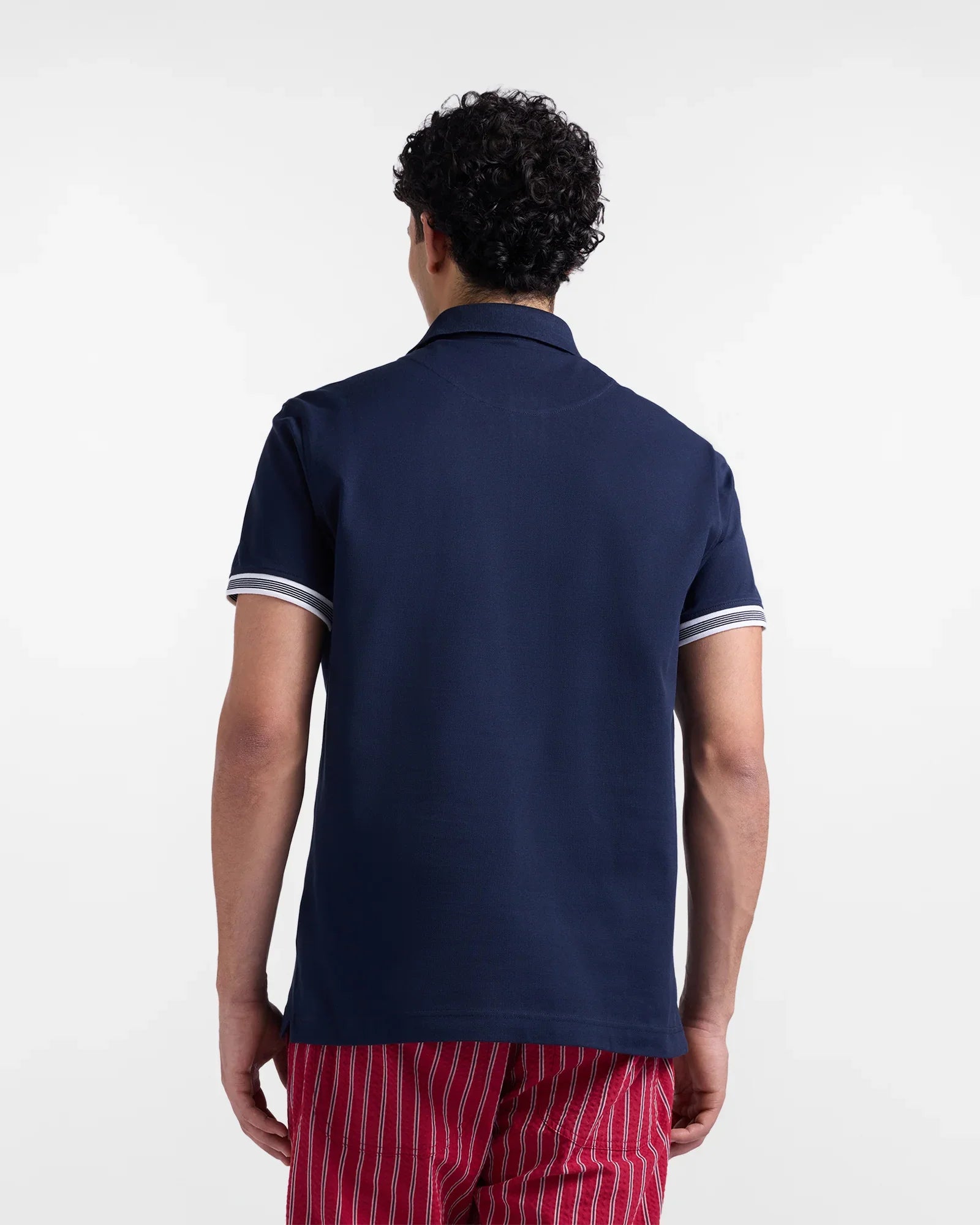 Uomo di spalle con polo blu a maniche corte e pantaloni rossi a righe bianche.