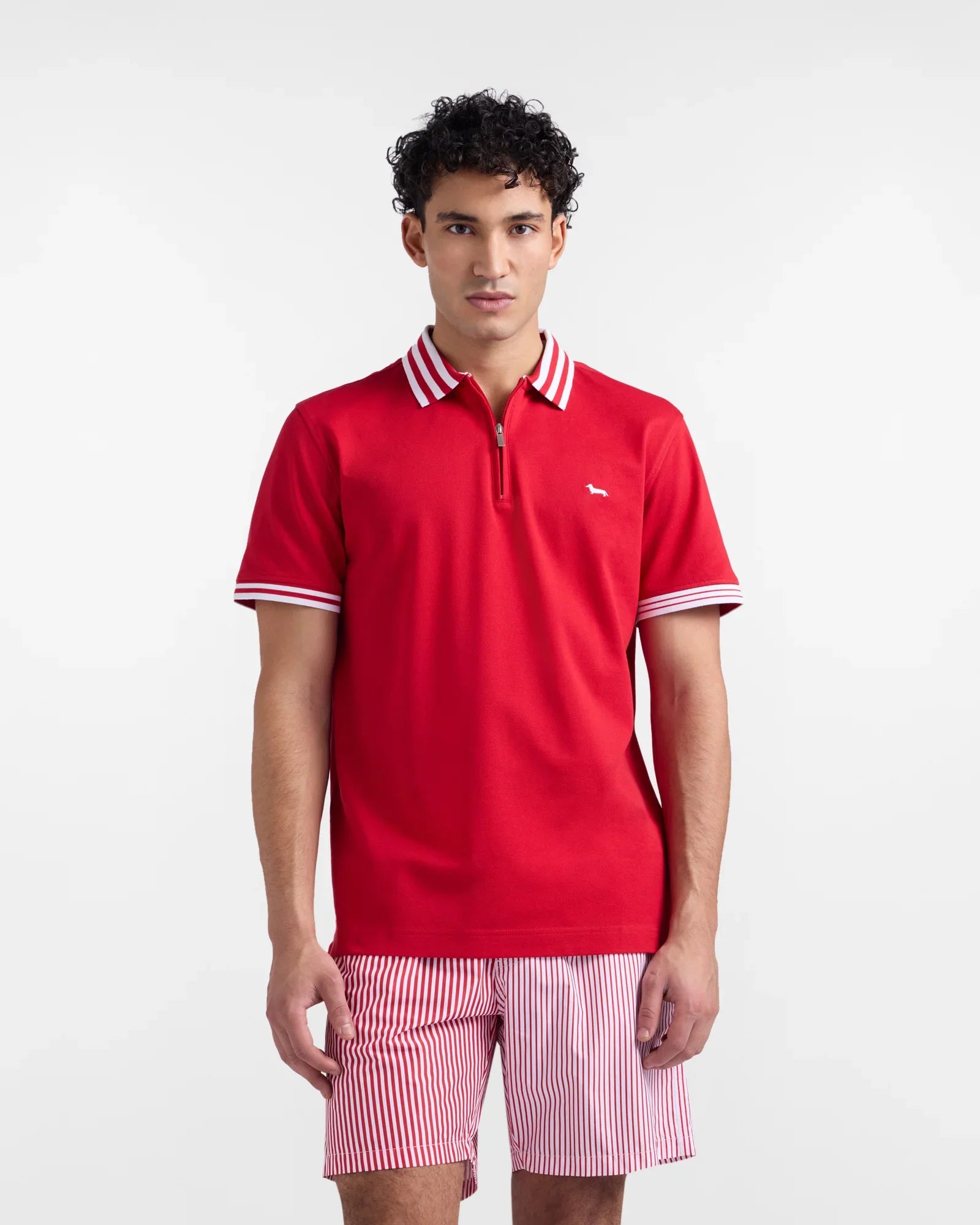 Uomo con polo rossa a maniche corte e colletto a righe, pantaloncini a righe rosse e bianche.