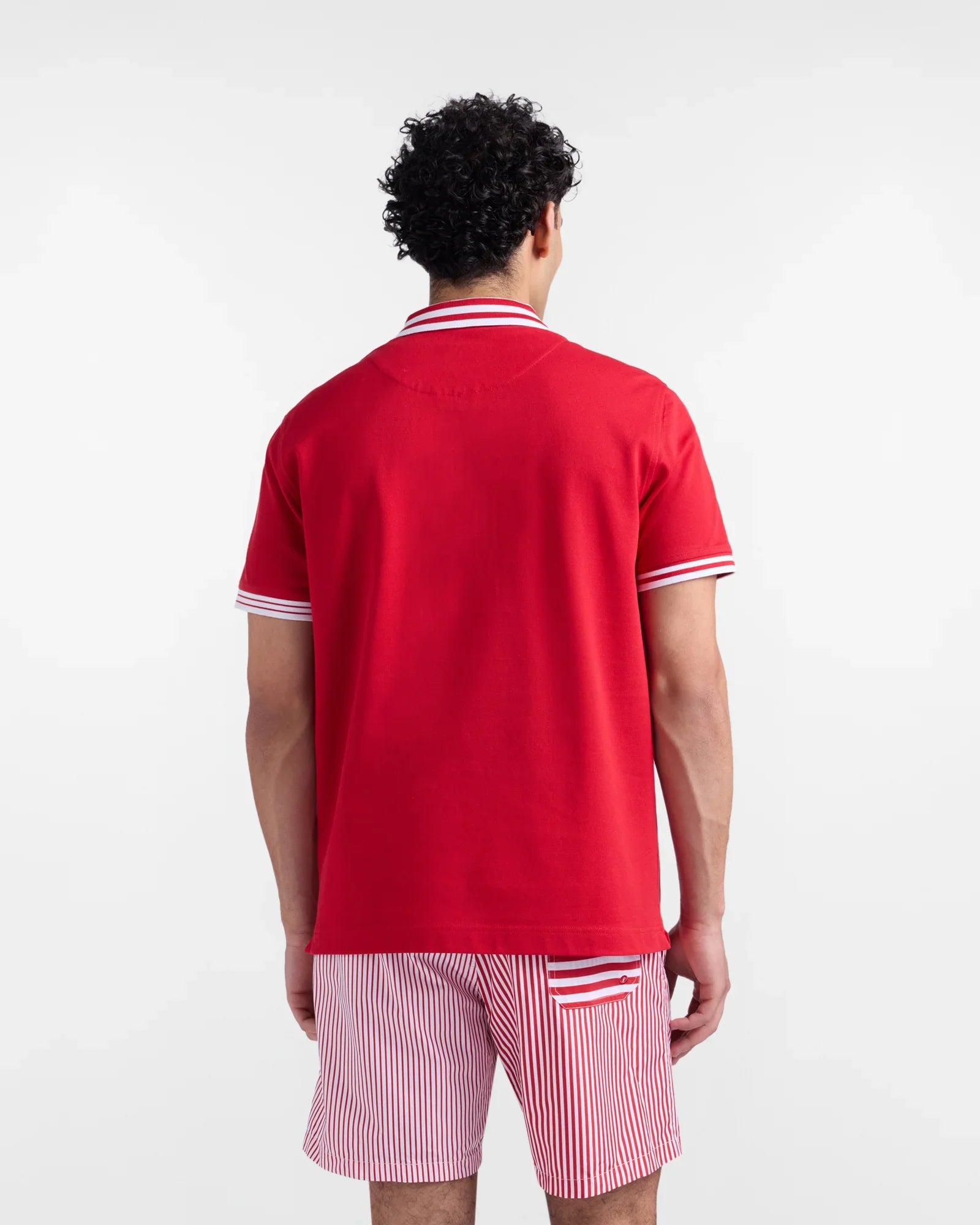 Uomo di spalle con polo rossa a maniche corte e pantaloncini a righe bianche e rosse