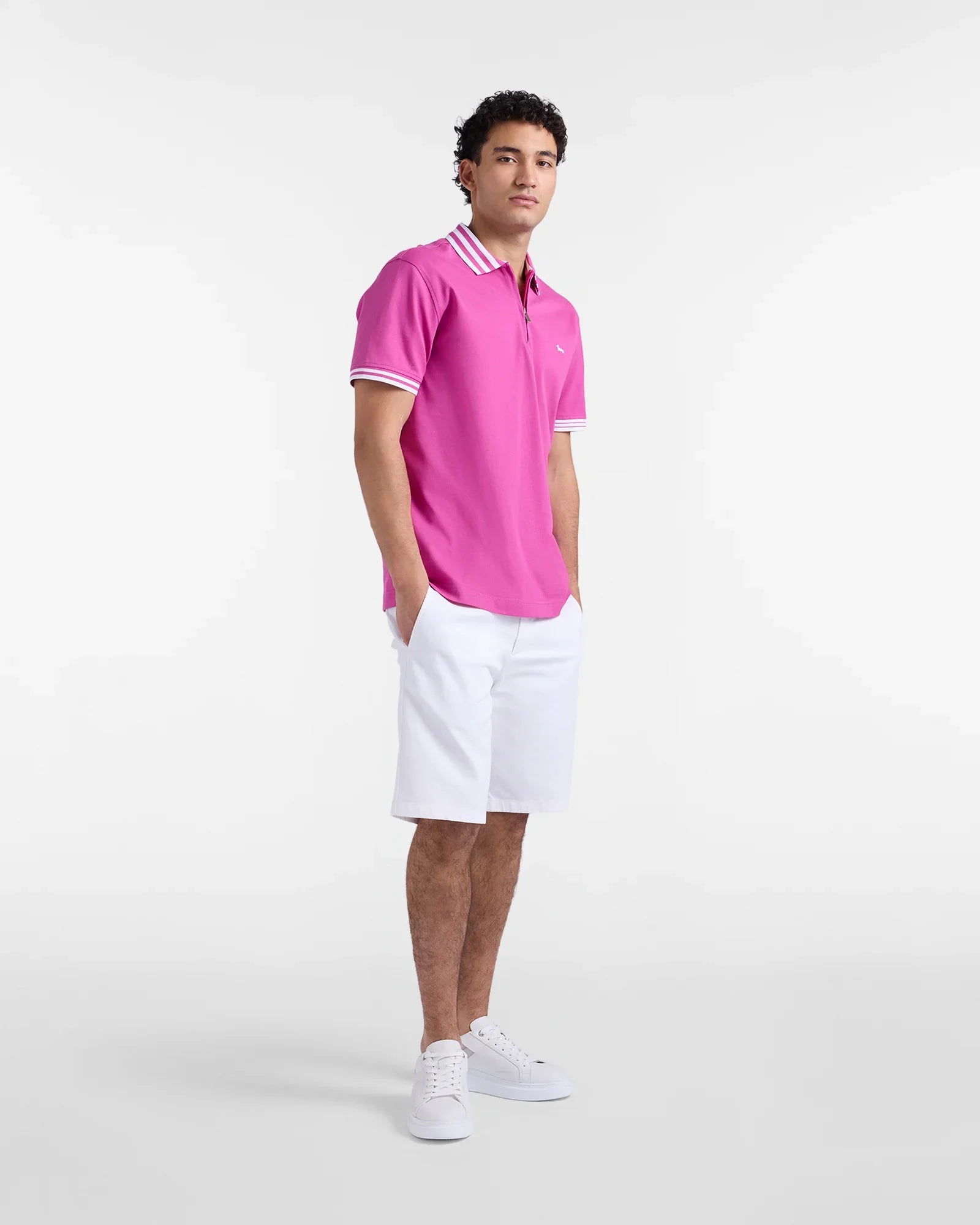 Uomo con polo fucsia, pantaloncini bianchi e sneakers bianche su sfondo neutro