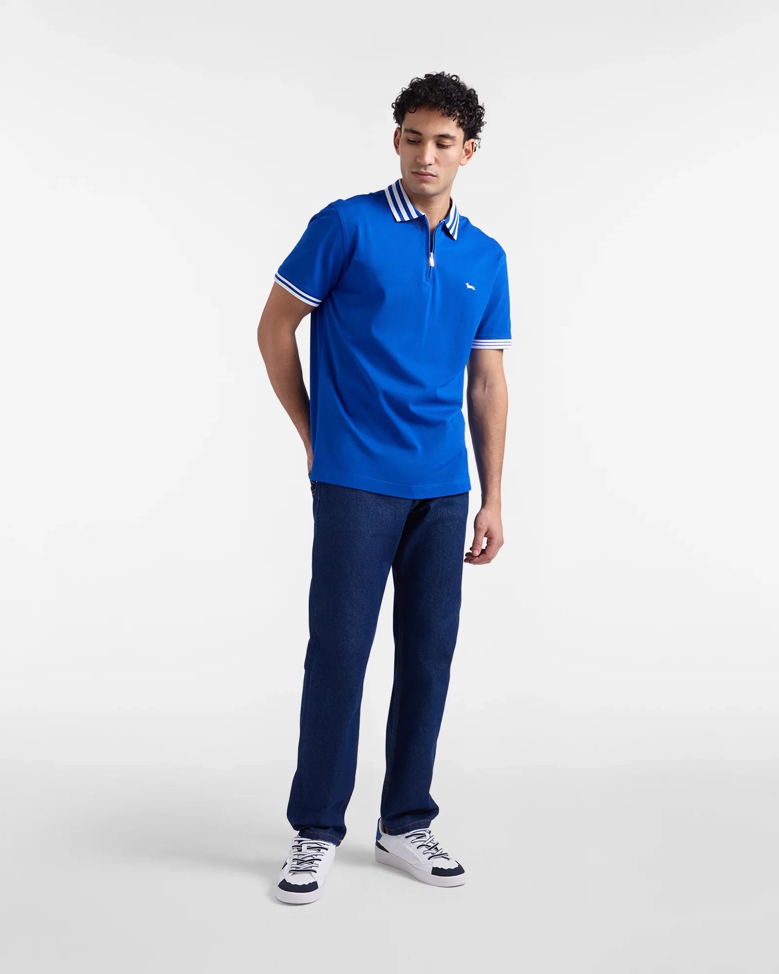 Modello indossa polo azzurra uomo a manica corta con colletto a righe, jeans blu e sneakers bianche.