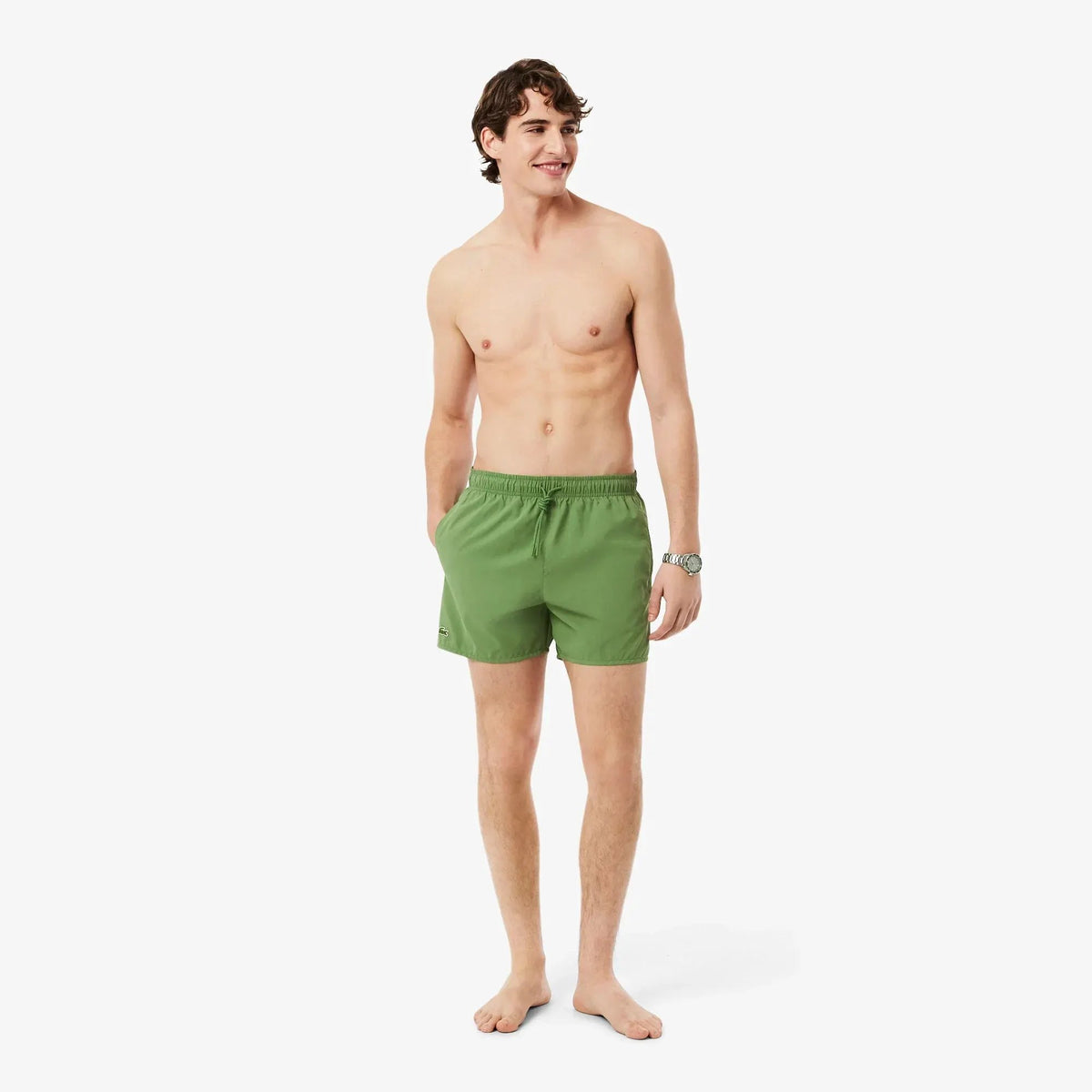 Modello uomo indossa costume da bagno verde corto, moda mare uomo, sfondo bianco.