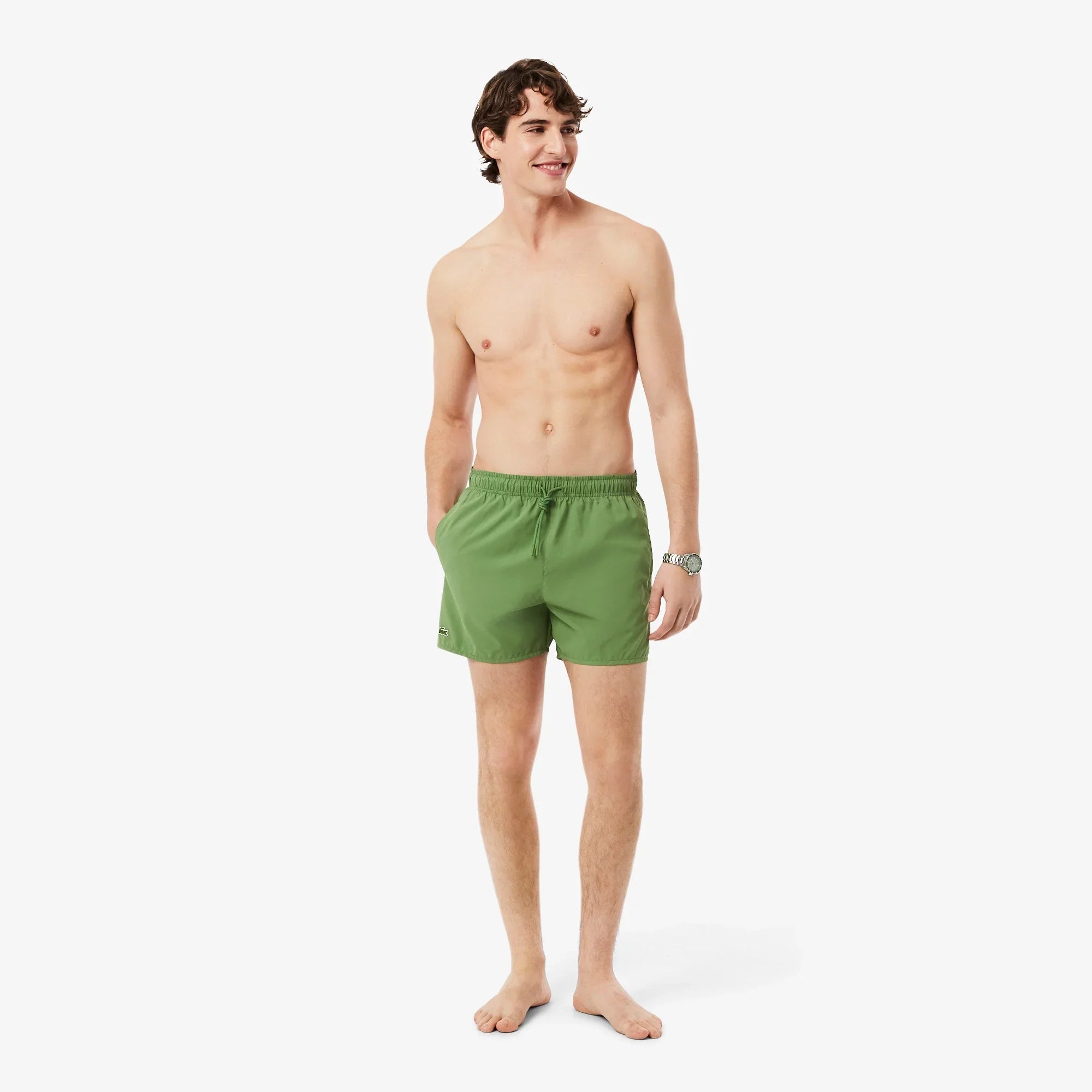 Modello uomo indossa costume da bagno verde corto, moda mare uomo, sfondo bianco.