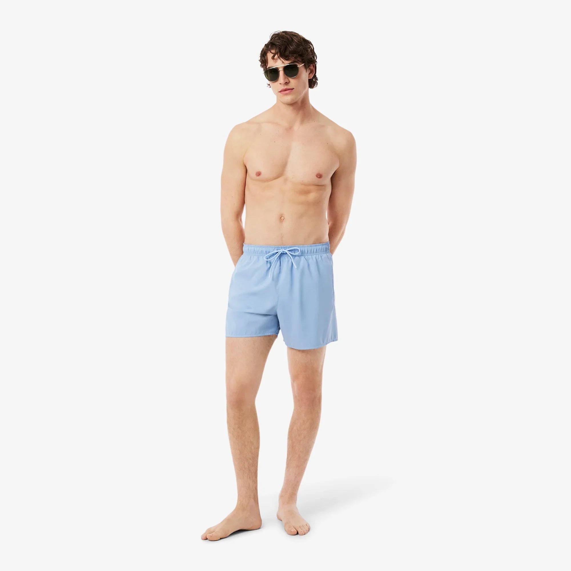 Uomo con occhiali da sole indossa boxer mare azzurri su sfondo bianco