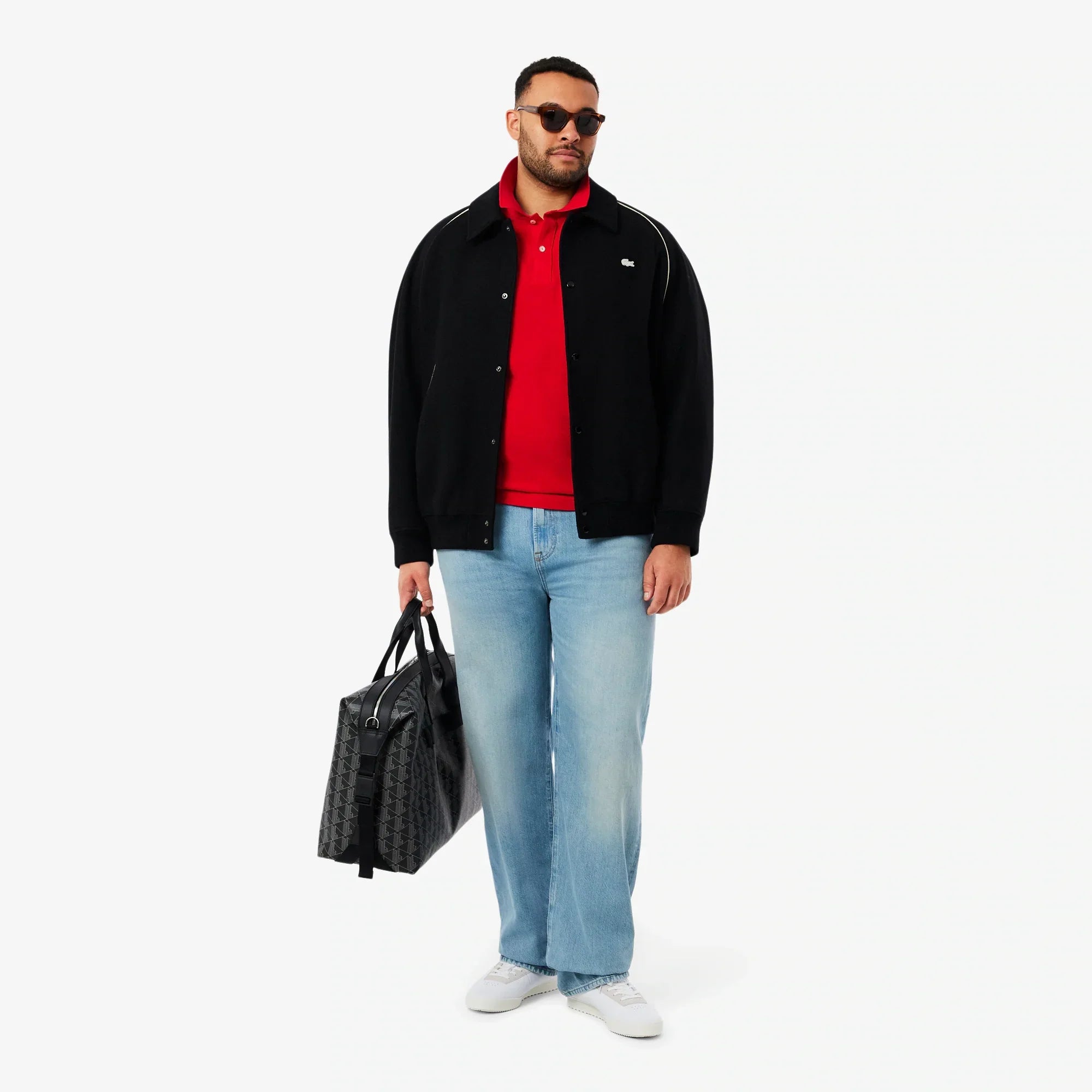 Uomo con giacca nera, polo rossa, jeans chiari, borsa nera e sneakers bianche