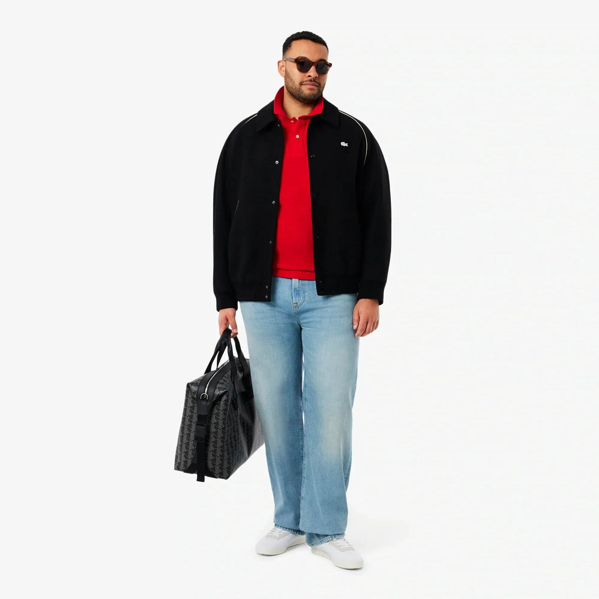 Uomo con giacca nera, polo rossa, jeans chiari, borsa nera e sneakers bianche