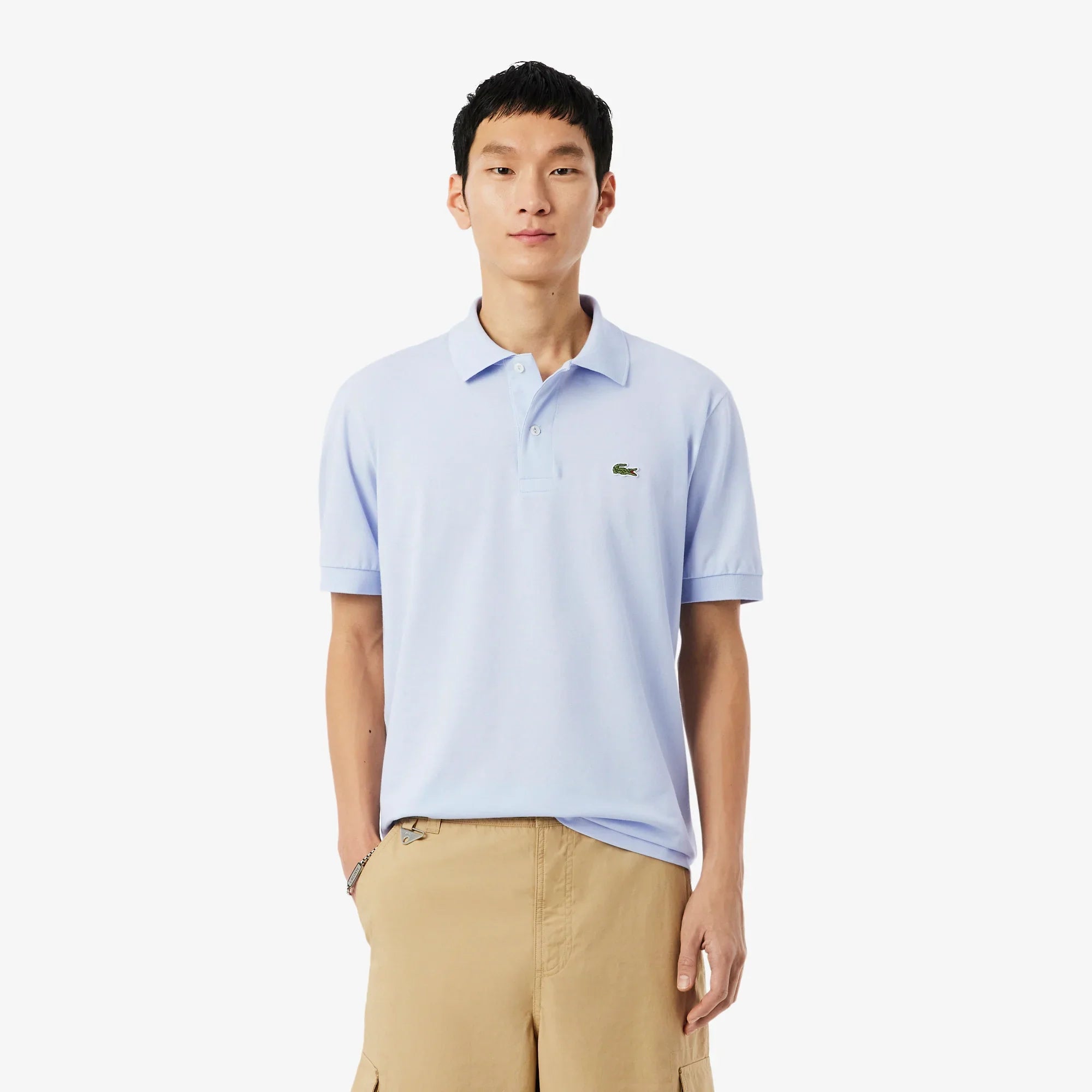 Uomo con polo celeste a manica corta e pantaloni beige, su sfondo bianco, moda uomo casual.