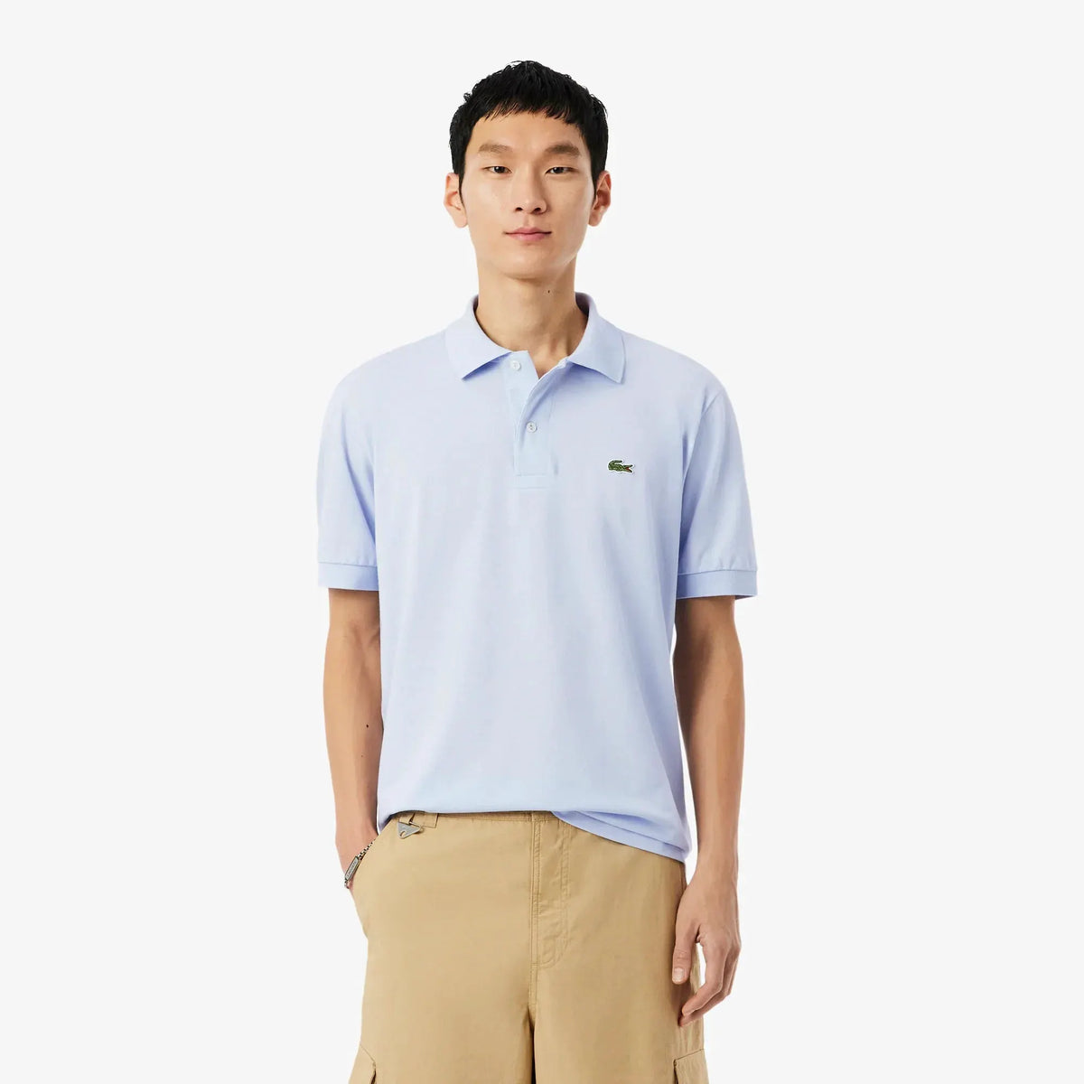 Uomo con polo celeste a manica corta e pantaloni beige, su sfondo bianco, moda uomo casual.