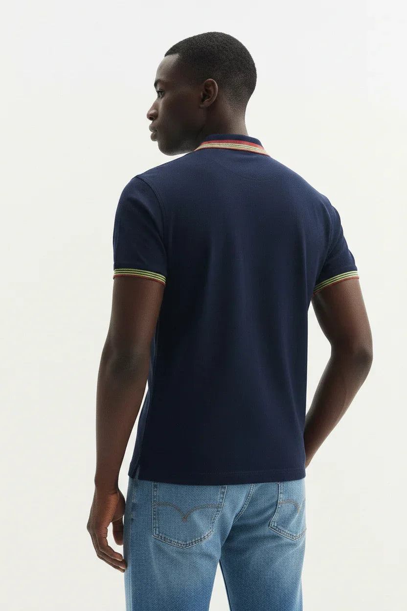 Uomo con polo blu manica corta con dettagli colorati sul colletto e sui polsini, jeans chiari.