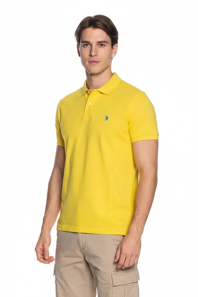 Modello uomo indossa polo gialla a maniche corte, pantaloni beige, sfondo bianco, stile casual.