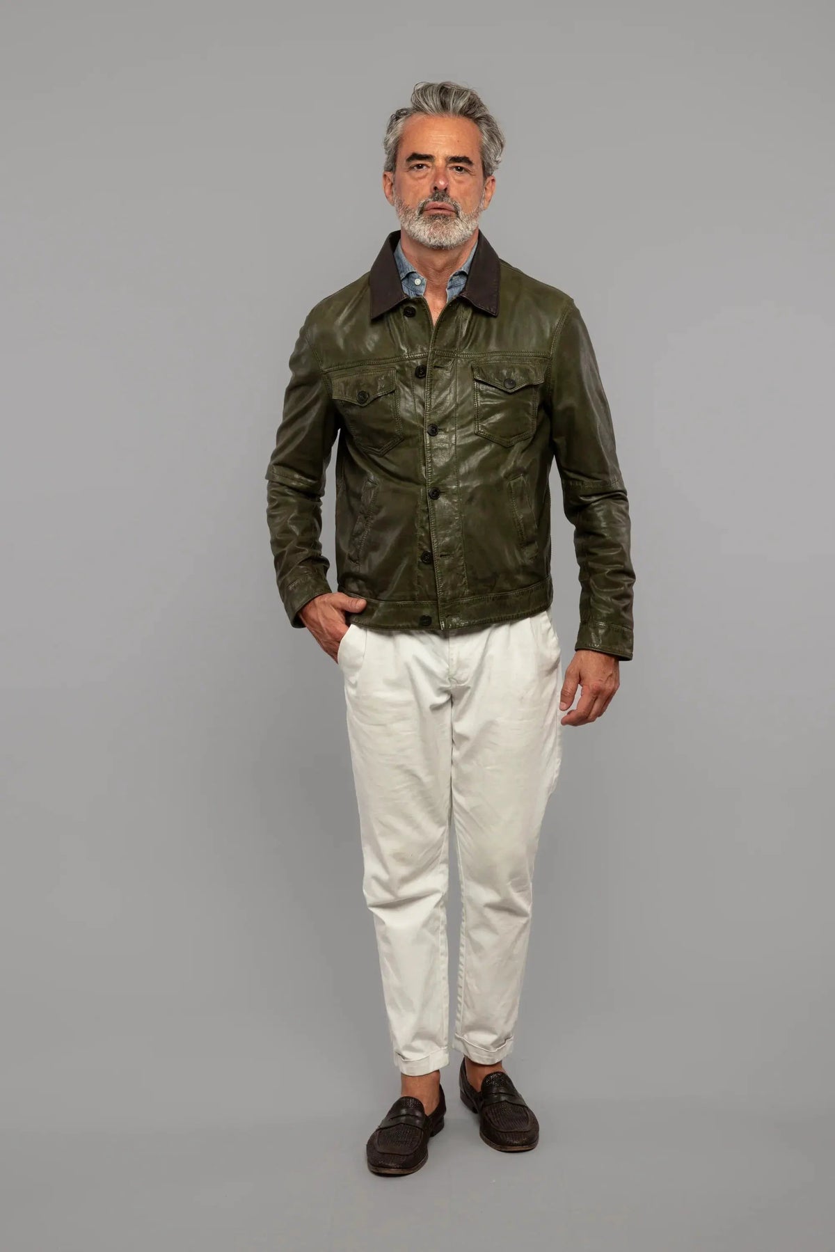 Uomo indossa giacca in pelle verde, camicia azzurra, pantaloni bianchi, mocassini scuri