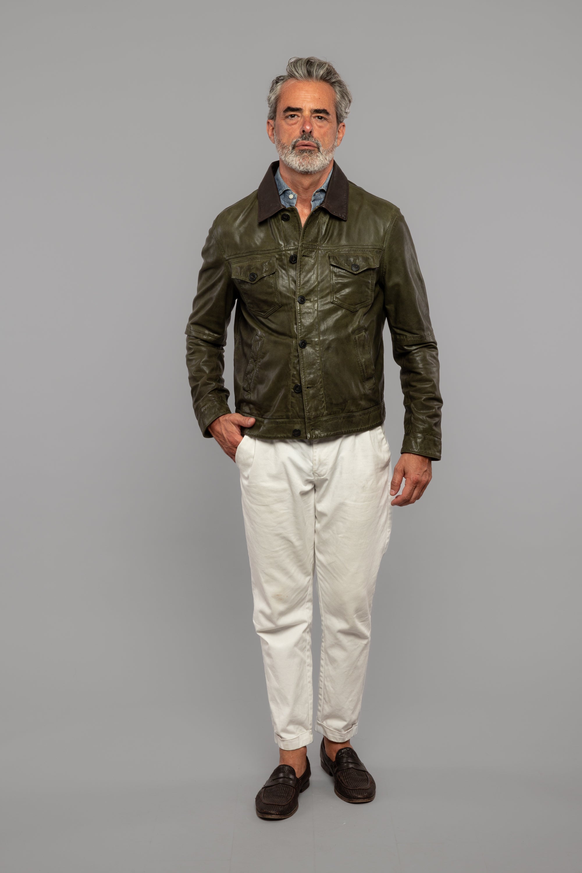 Uomo indossa giacca in pelle verde, camicia azzurra, pantaloni bianchi, mocassini scuri
