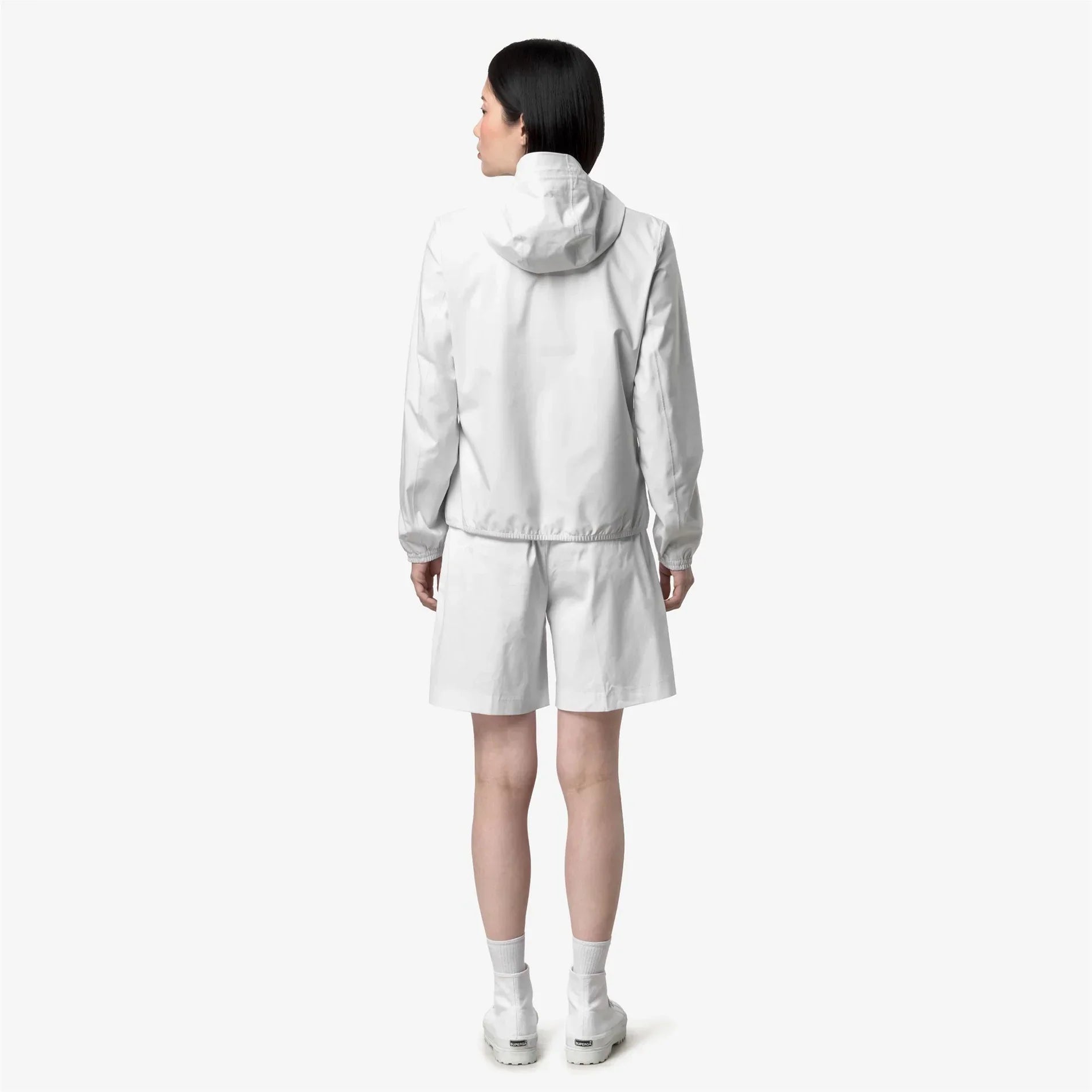 Donna di spalle indossa giacca con cappuccio e pantaloncini bianchi, look sportivo minimalista