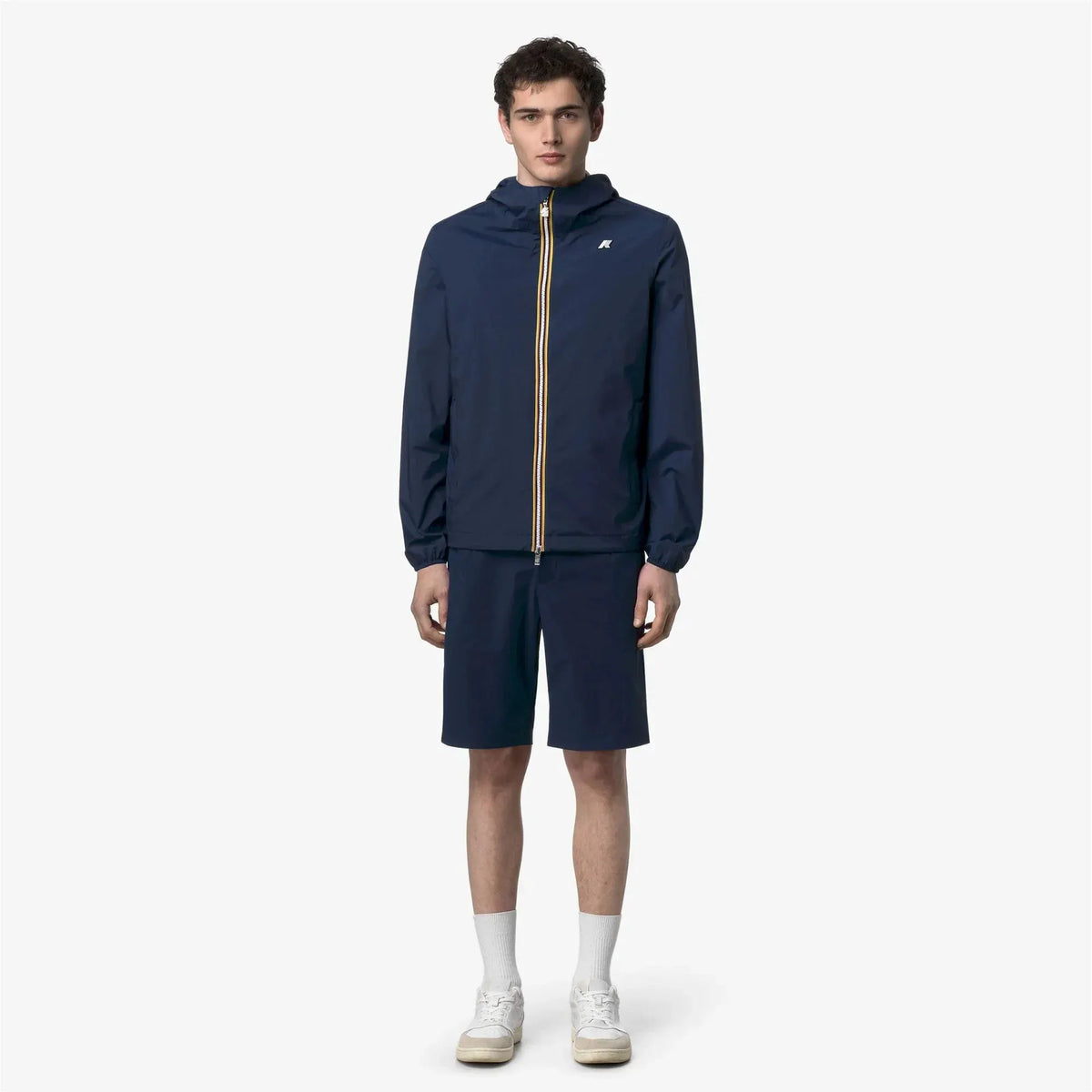 Modello uomo con giacca leggera blu con cappuccio e pantaloncini, look casual estivo