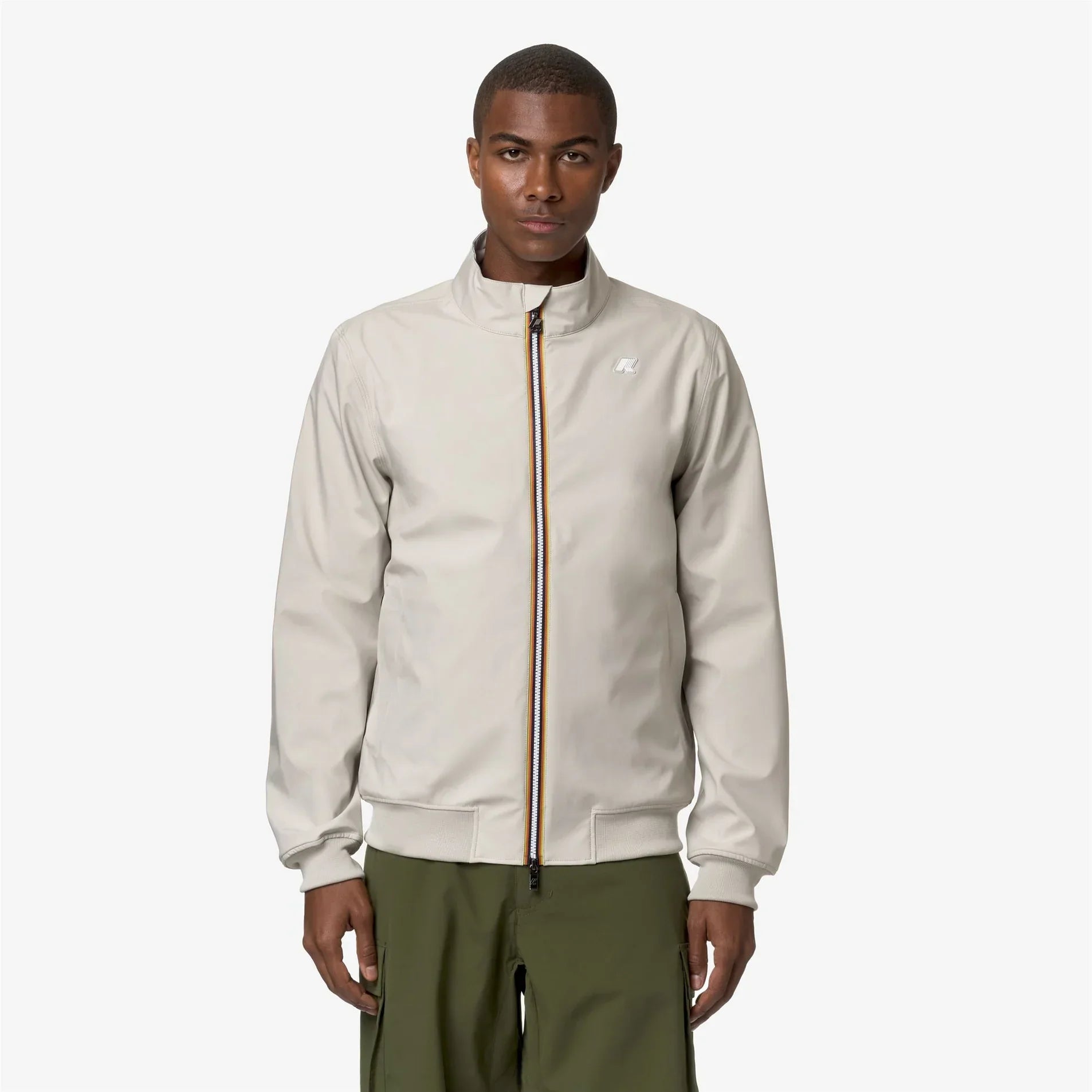 Giacca uomo beige con zip centrale a contrasto, modello casual elegante, indossata su pantaloni verdi.