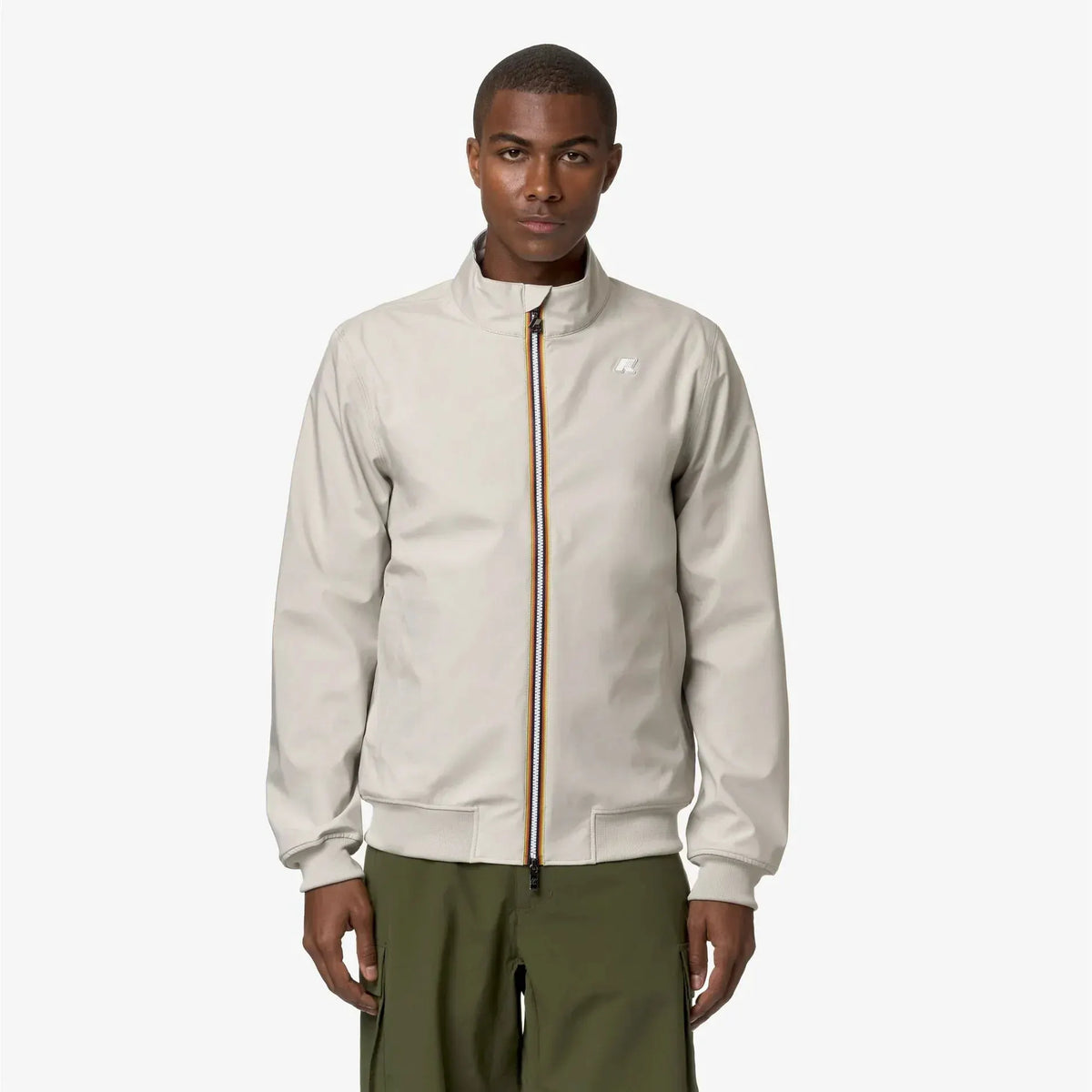 Giacca uomo beige con zip centrale a contrasto, modello casual elegante, indossata su pantaloni verdi.