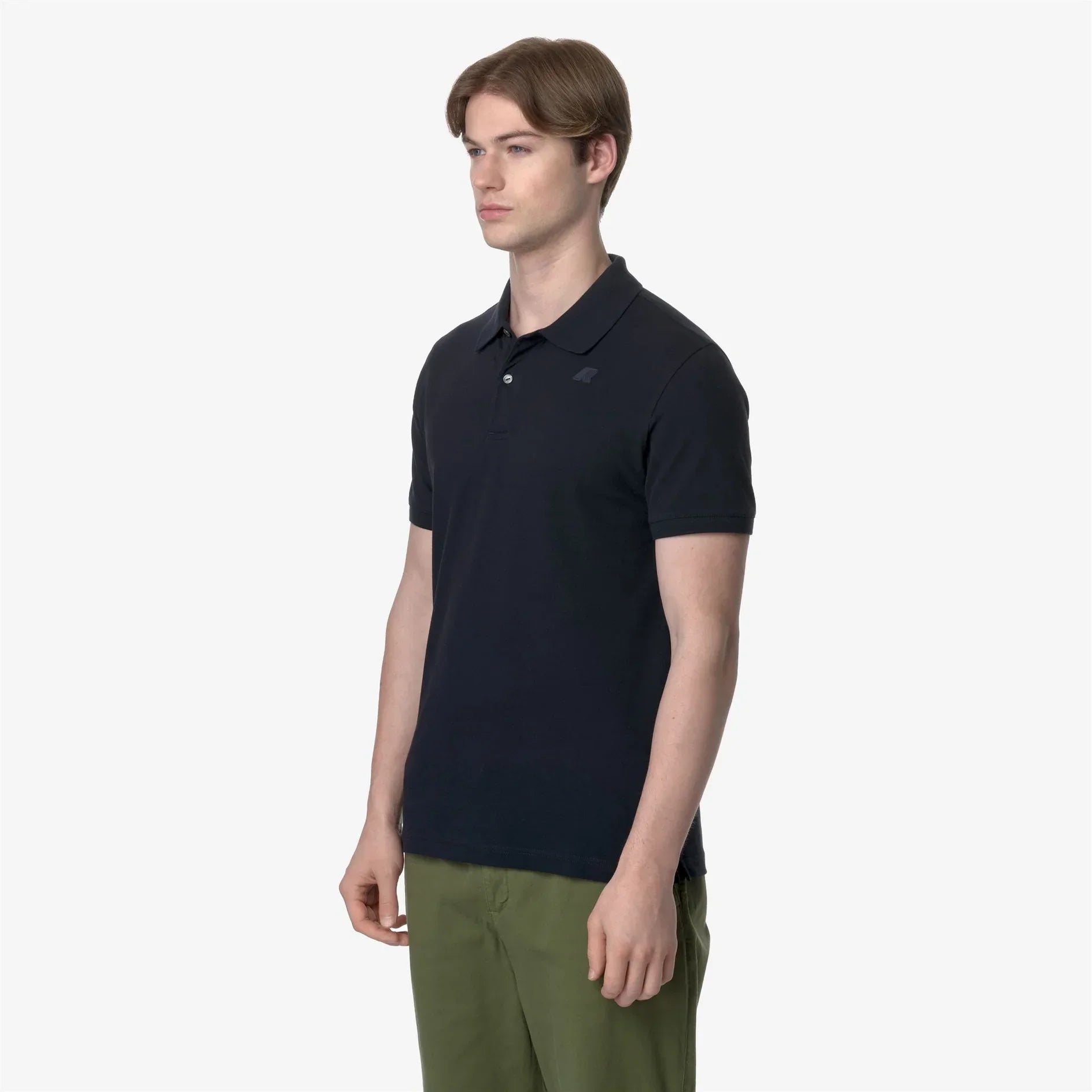 Modello indossa polo nera da uomo a maniche corte con pantaloni verdi, sfondo chiaro