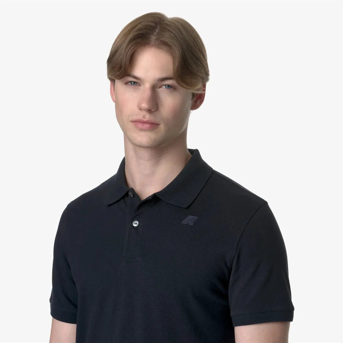 Uomo con polo nera a manica corta, stile casual elegante, sfondo neutro.