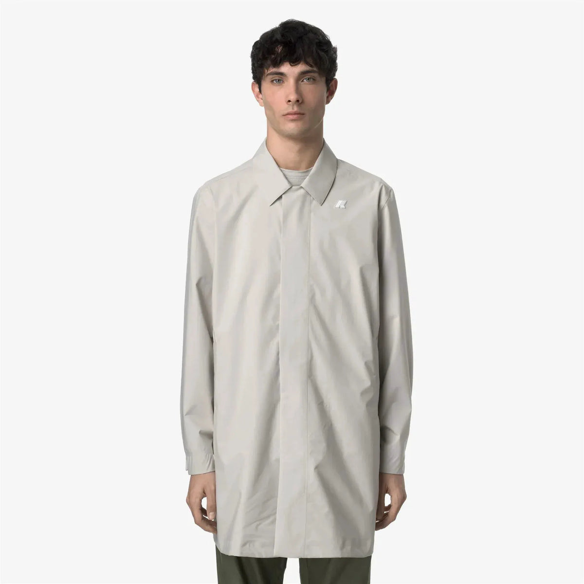 Modello indossa soprabito uomo beige chiaro, design minimal, su sfondo bianco.