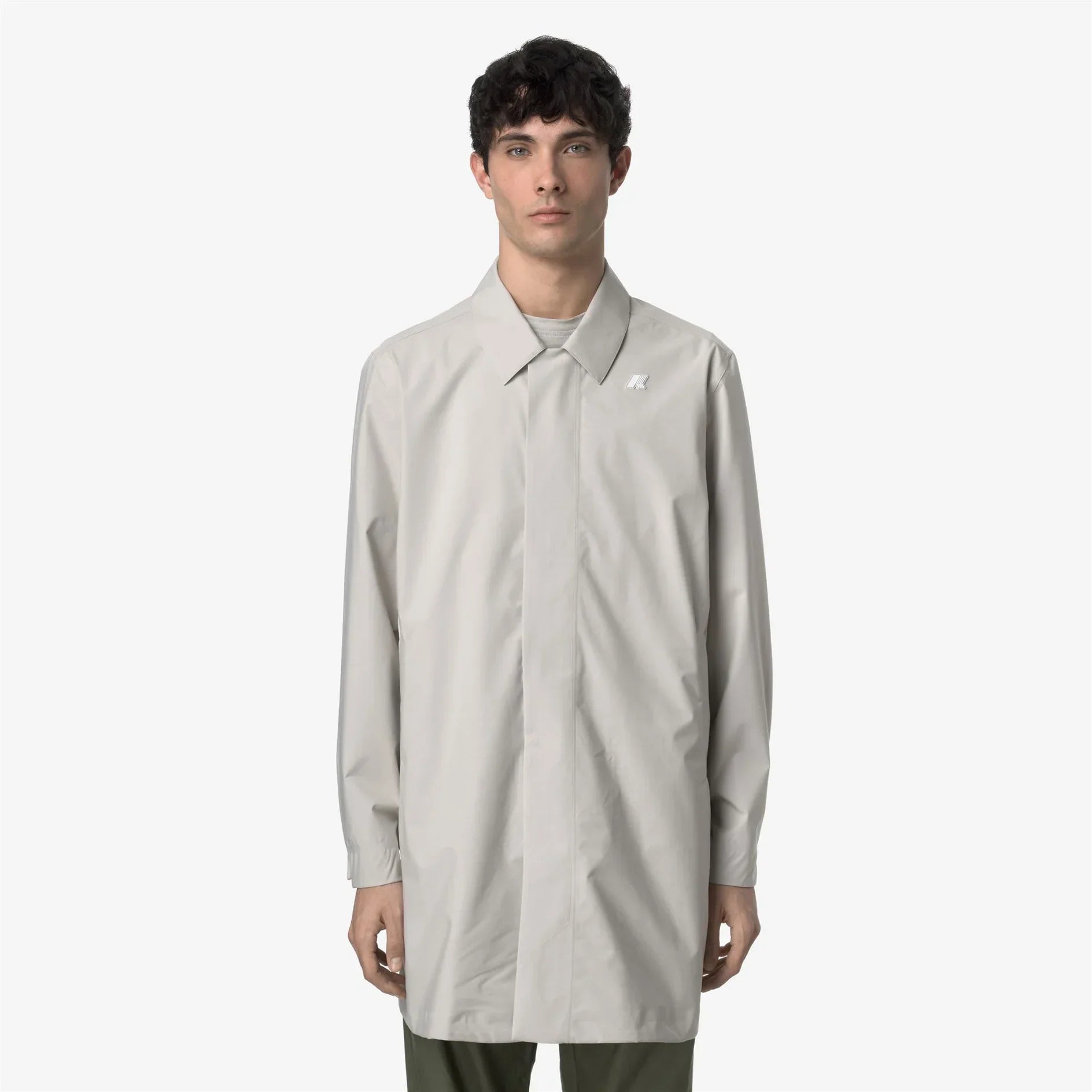 Modello indossa soprabito uomo beige chiaro, design minimal, su sfondo bianco.