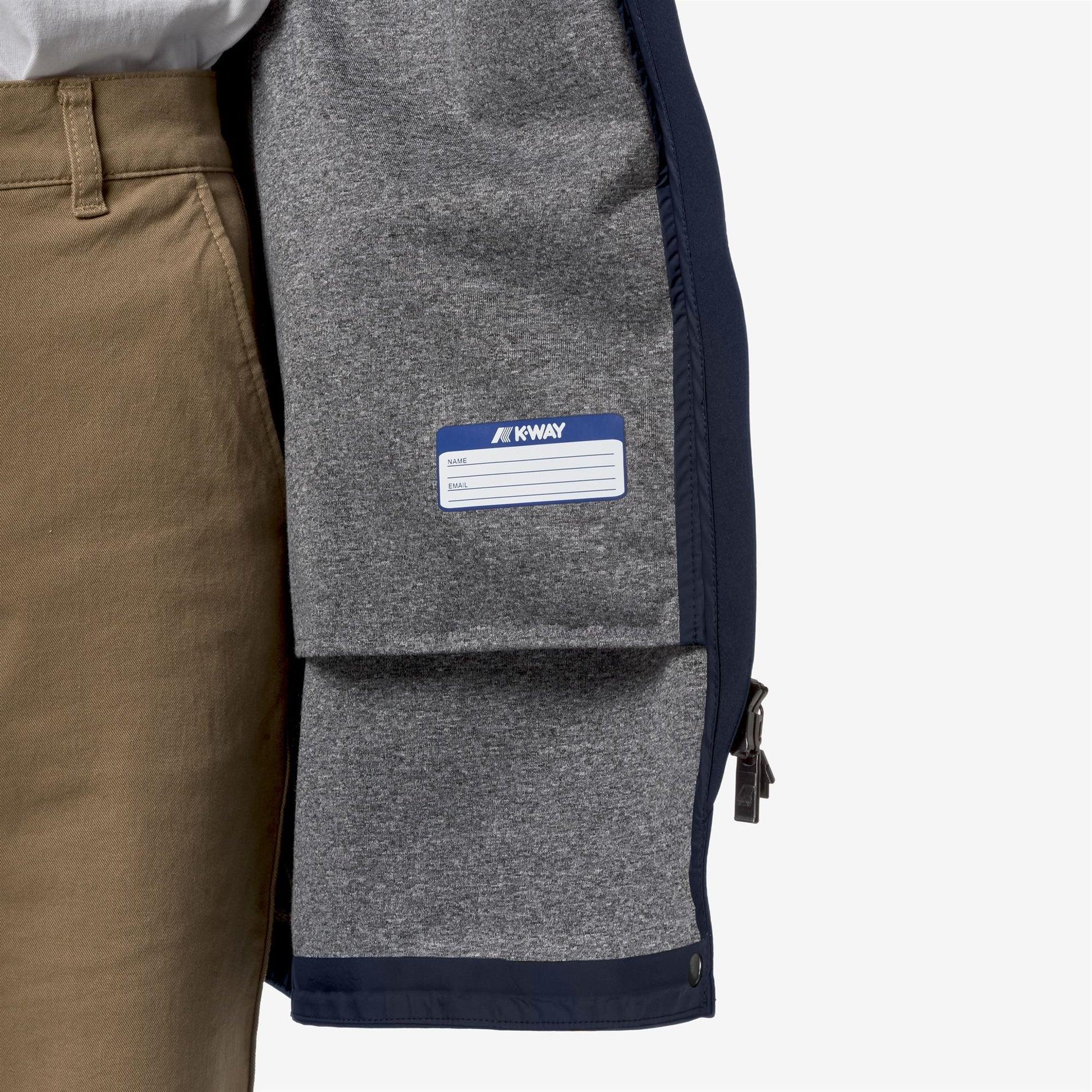 Interno giacca K-Way blu e grigia con etichetta identificativa, dettaglio su tessuto e zip.