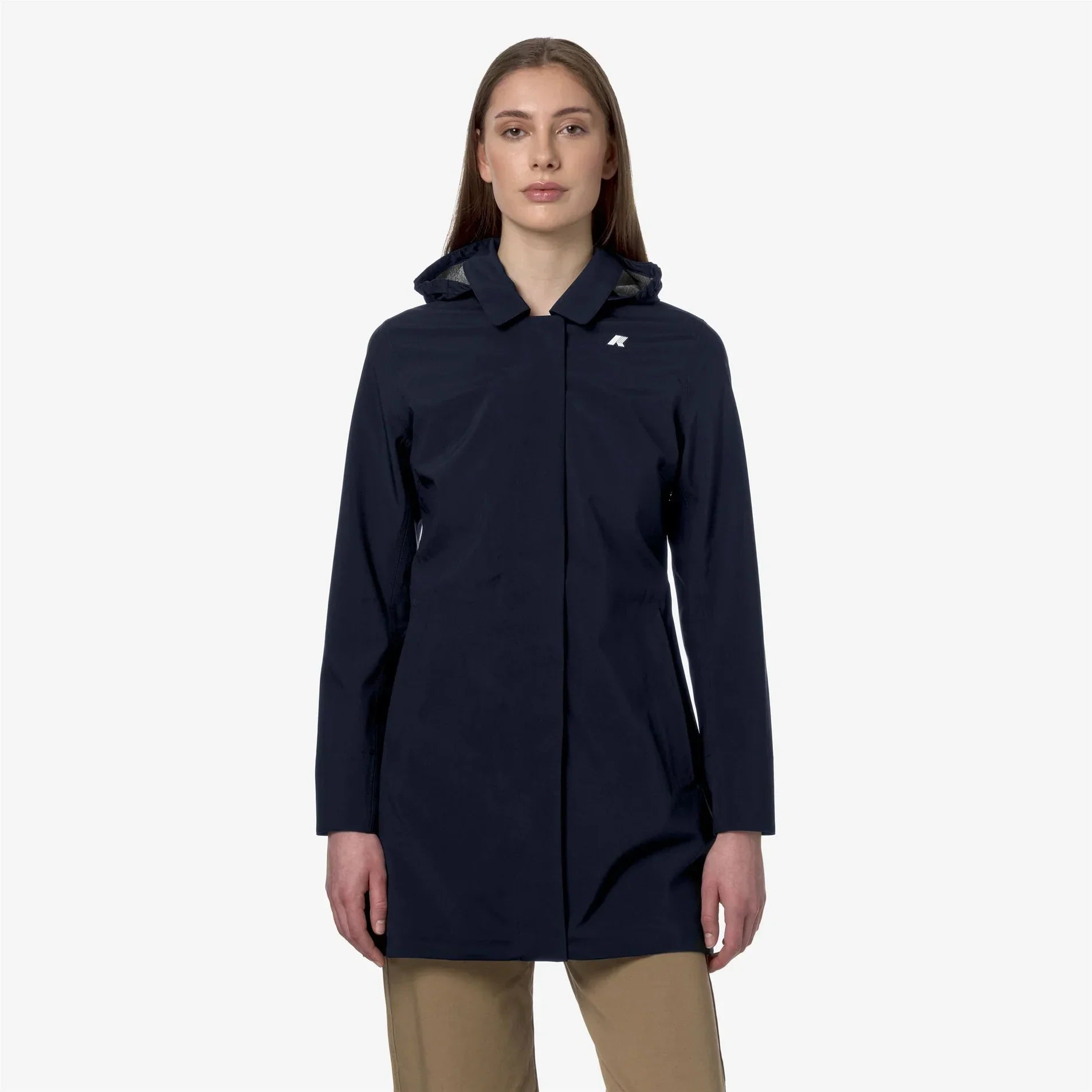 Donna indossa parka impermeabile blu scuro con cappuccio e pantaloni beige, fondo chiaro.