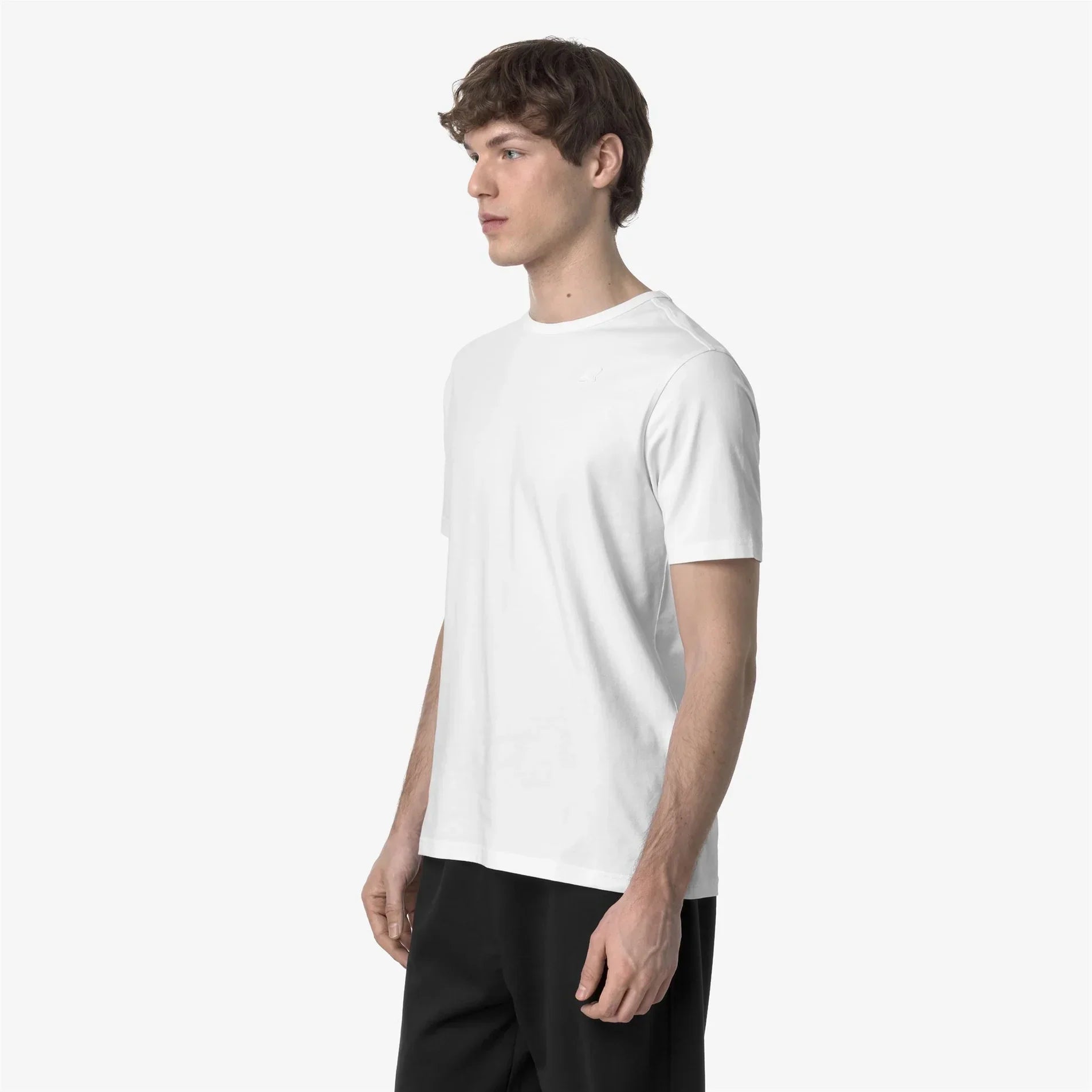 Giovane uomo indossa t-shirt bianca basic e pantaloni neri su sfondo neutro