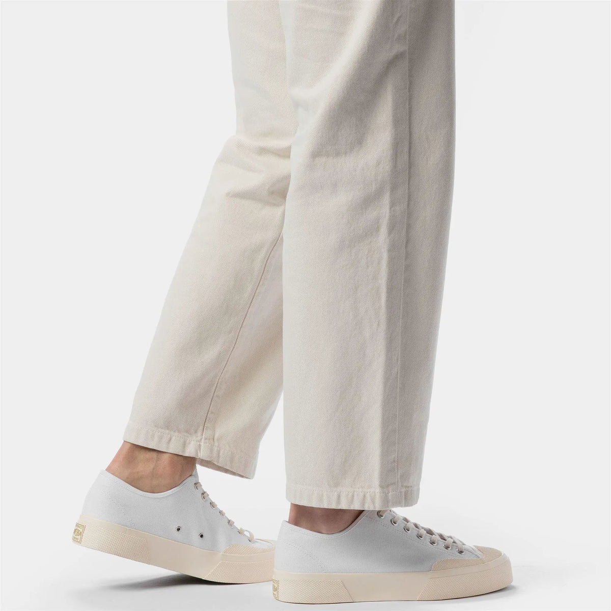 Sneakers bianche basse da uomo abbinate a pantaloni chiari, moda casual elegante