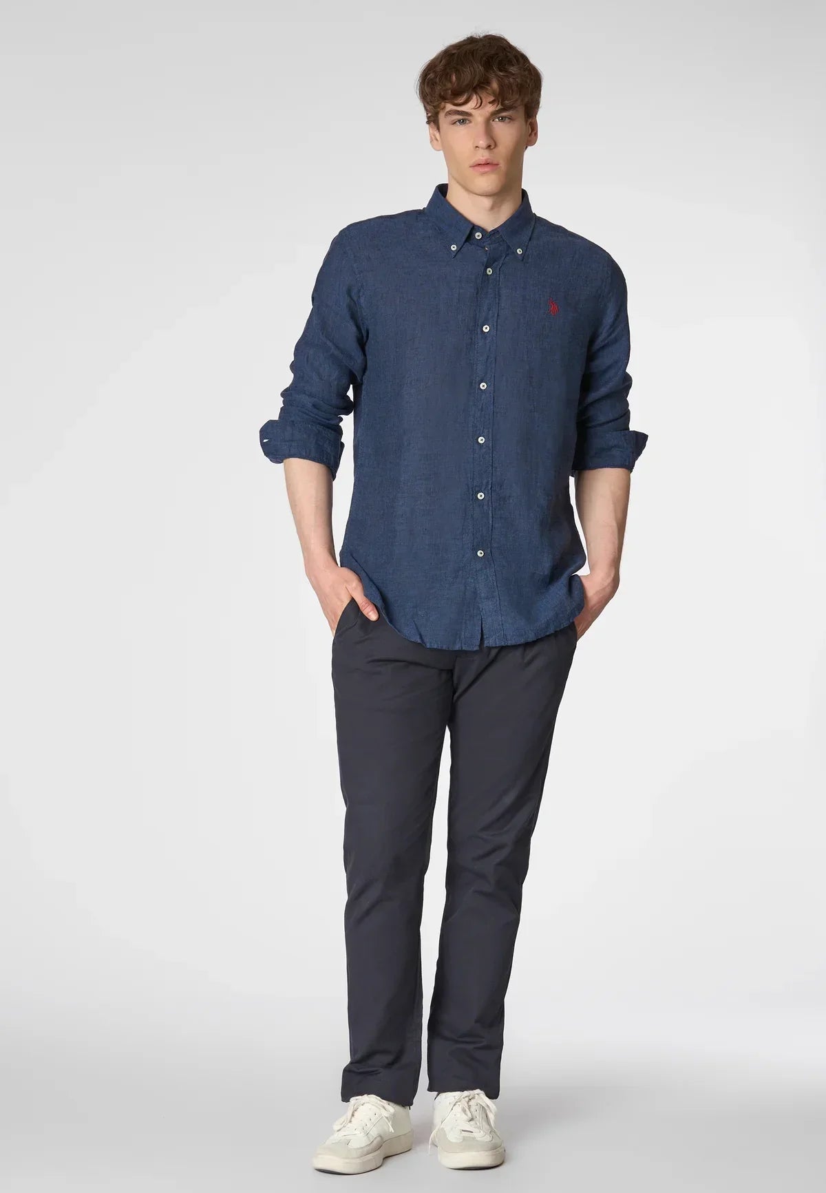 Modello uomo con camicia lino blu, pantaloni scuri e sneakers bianche, moda casual elegante.
