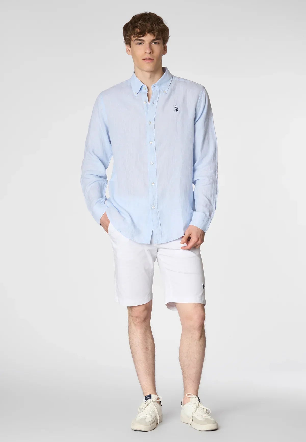 Modello indossa camicia azzurra a maniche lunghe e bermuda bianchi uomo, look casual estivo